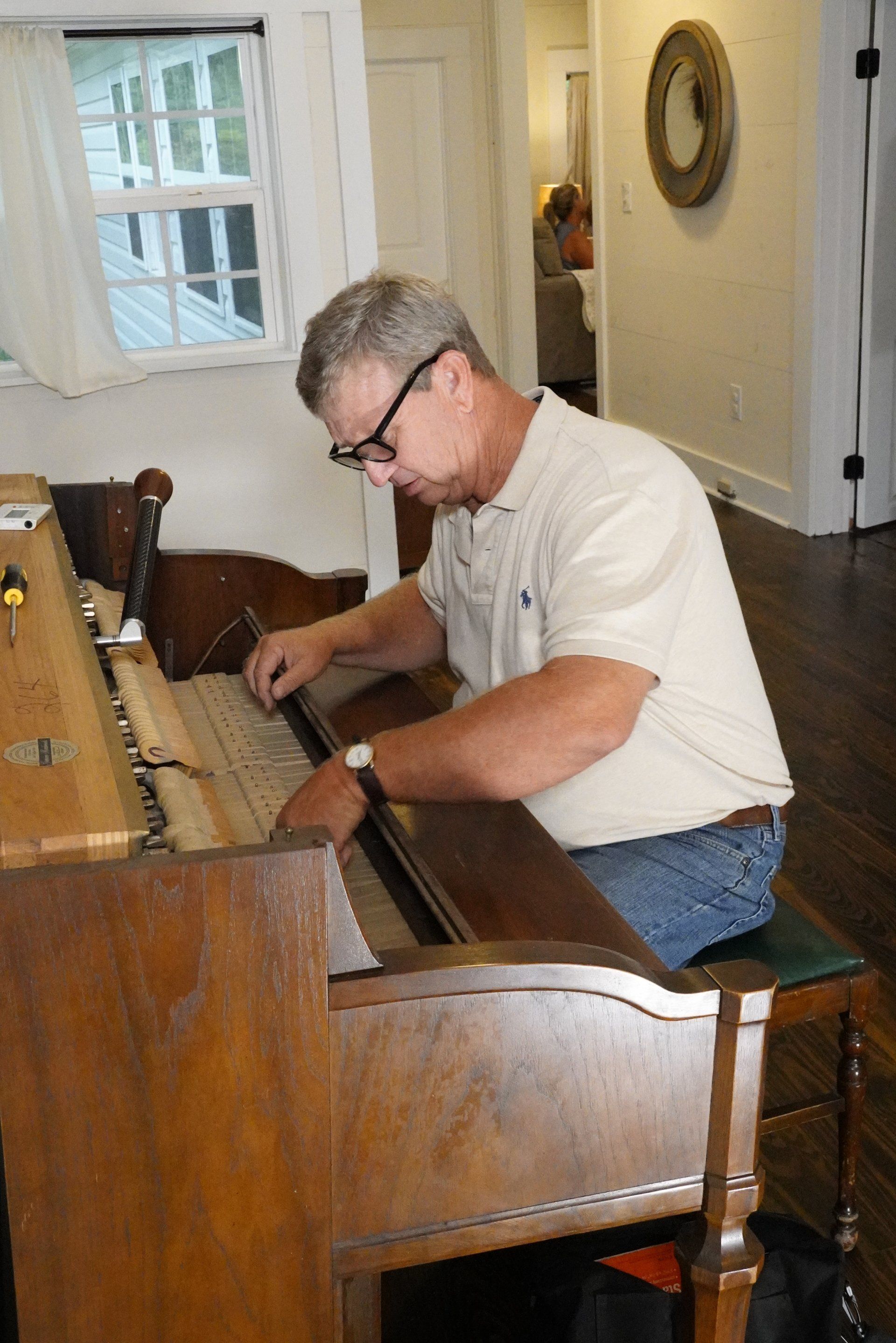 A man is sitting at a piano in a living room.