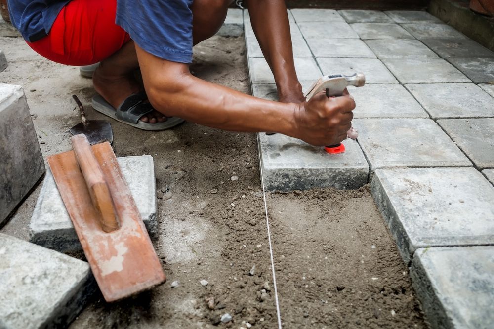 Person laying paving stones with a hammer in an outdoor setting.