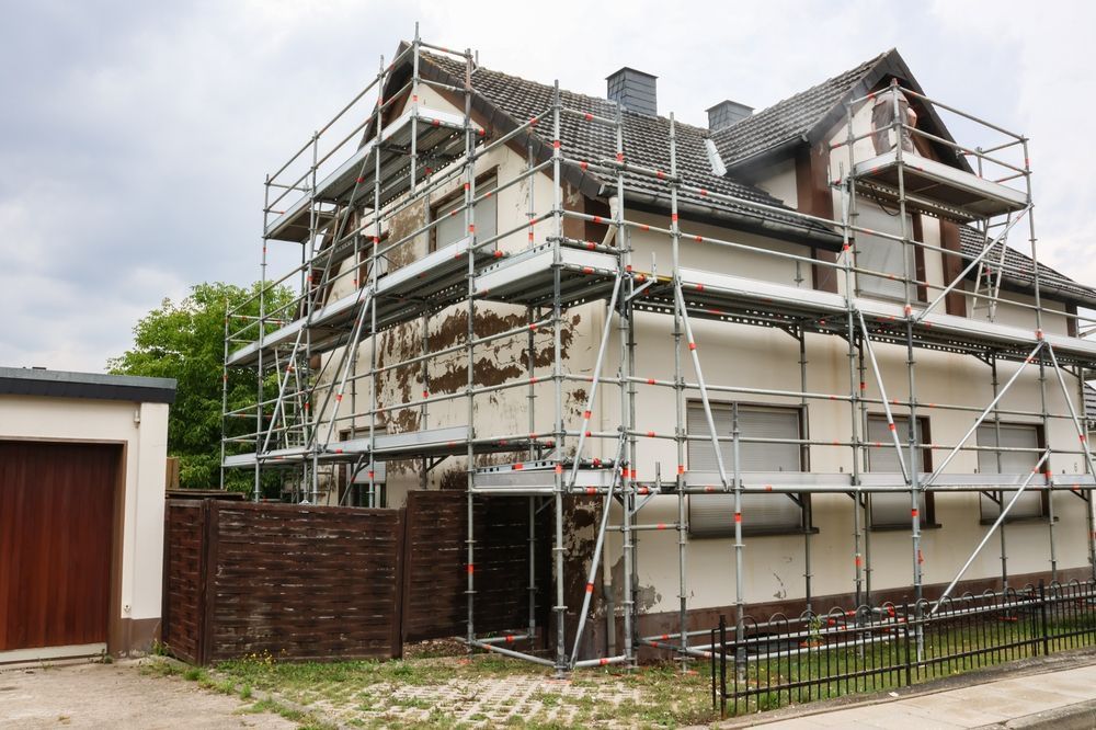 House under renovation with scaffolding, peeling paint on the white exterior, and brick fence.