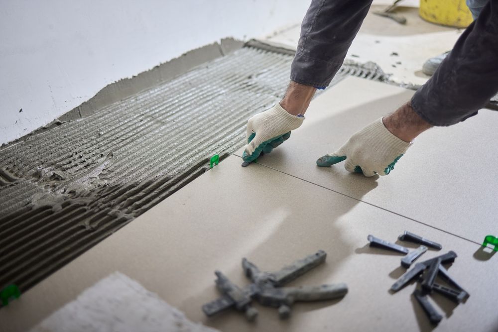 Person in gloves installing floor tiles, applying mortar.