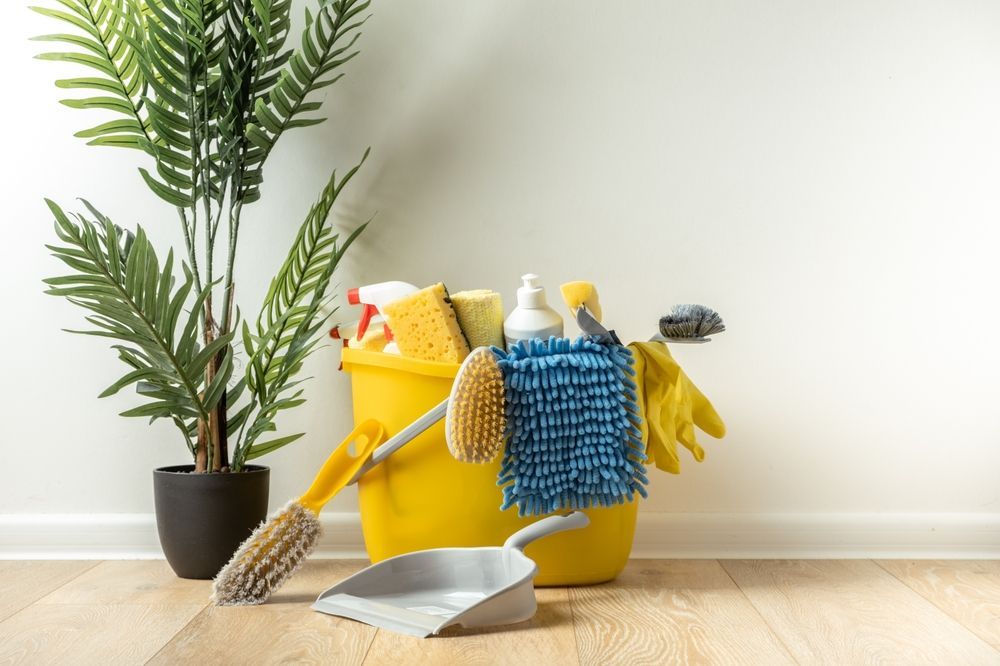 Yellow cleaning bucket with supplies, next to a potted plant, on a hardwood floor.