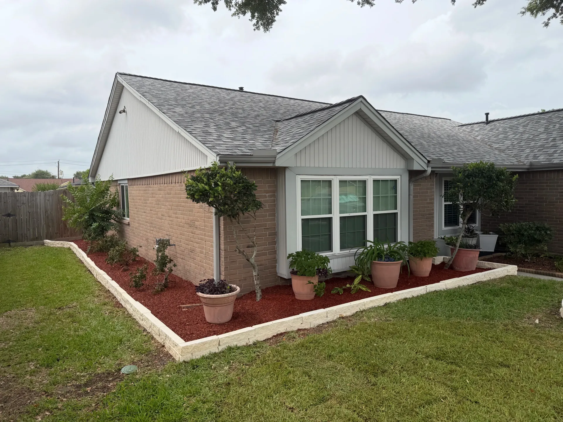 Single-story suburban house with brick exterior, gray roof, and a landscaped front yard with potted plants.