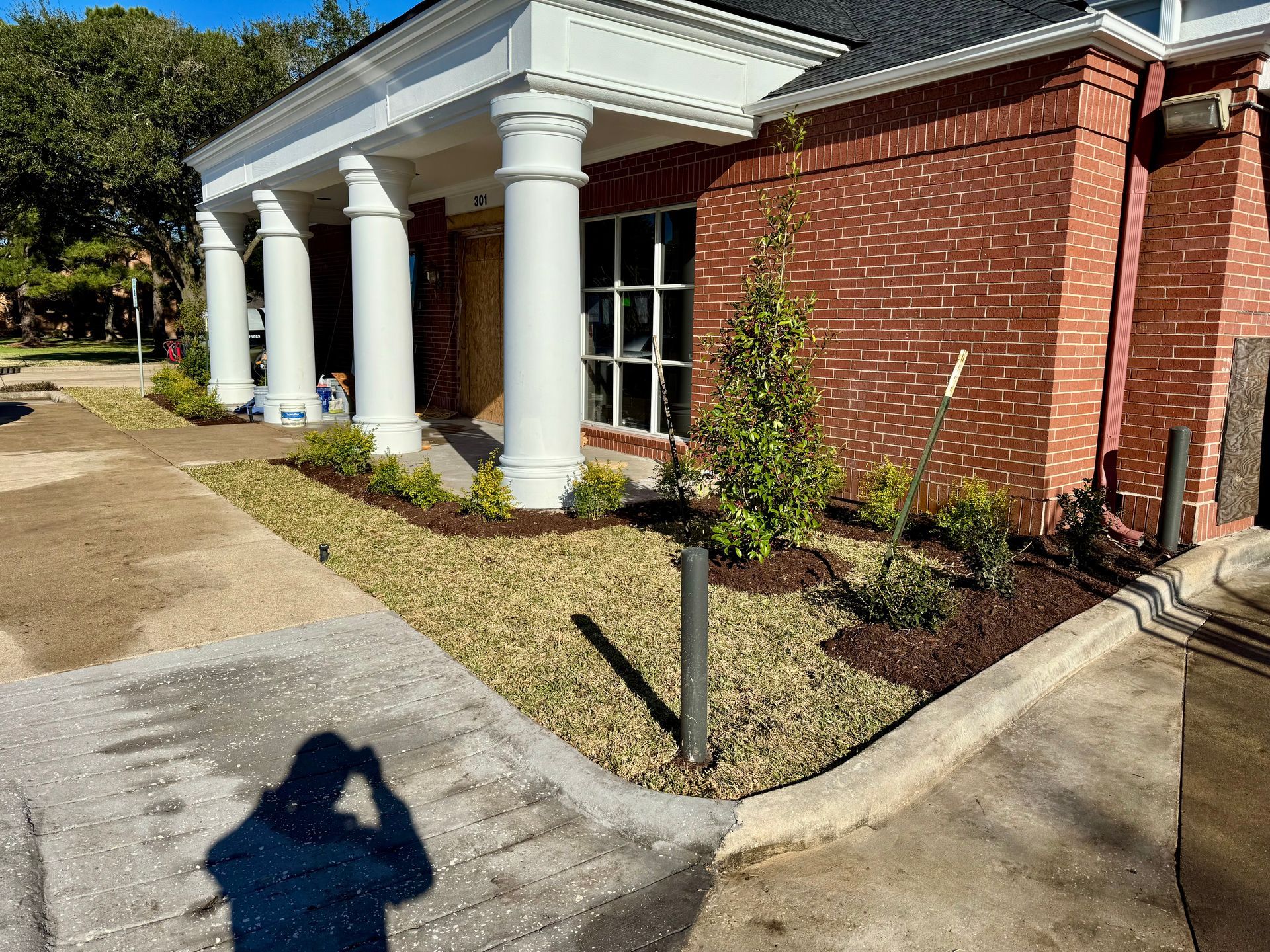 Building exterior with columns and brick, landscaped with bushes and mulch.