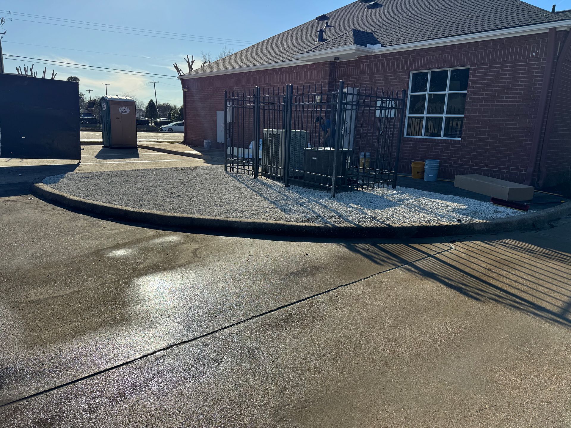 A person planting shrubs in a gravel-covered garden. The setting is enclosed, with a brown wall and green plants.
