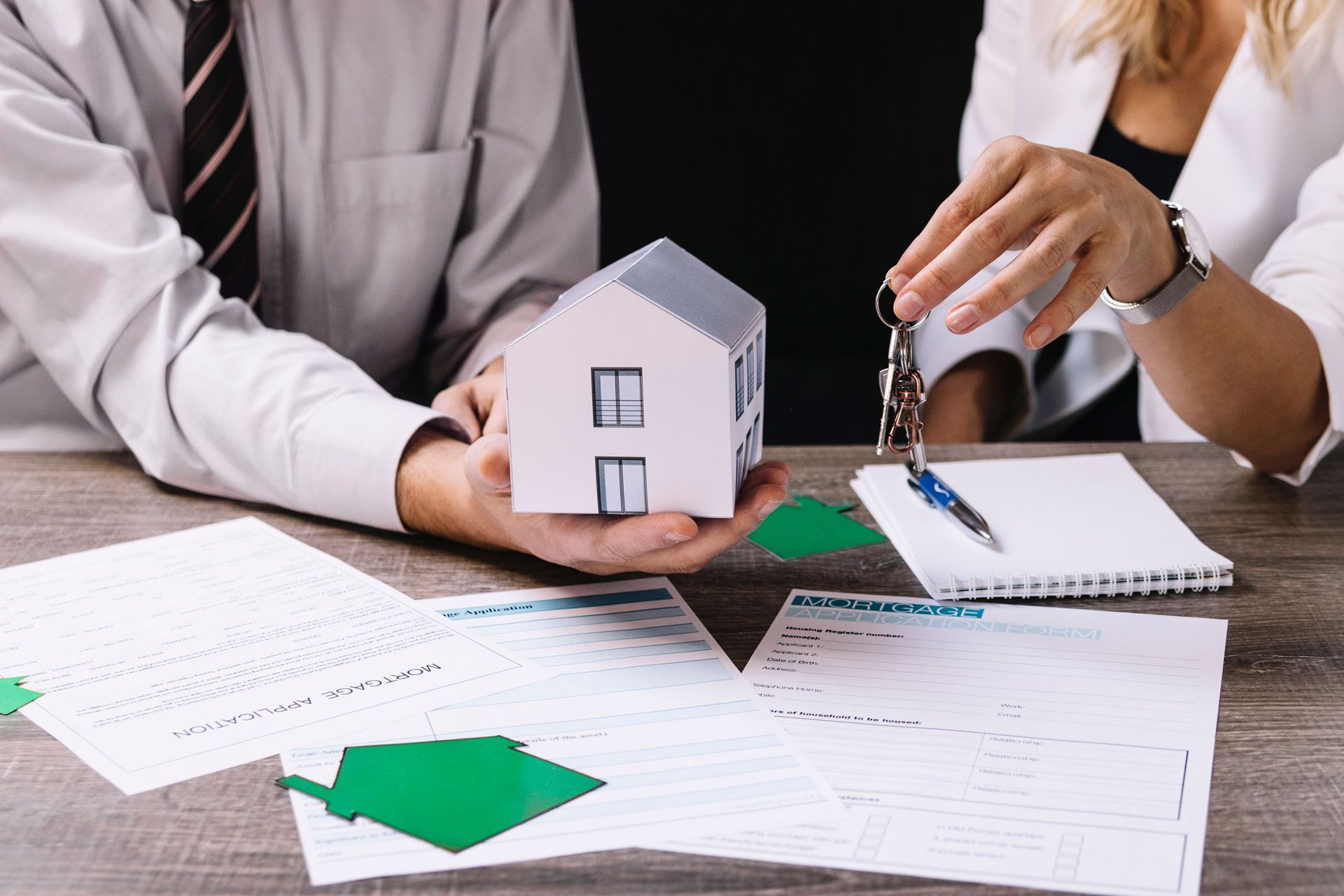 Two people with paperwork, a house model, and keys; real estate transaction.