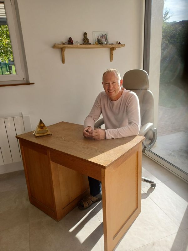un homme est assis à un bureau en bois dans une pièce avec une grande fenêtre .