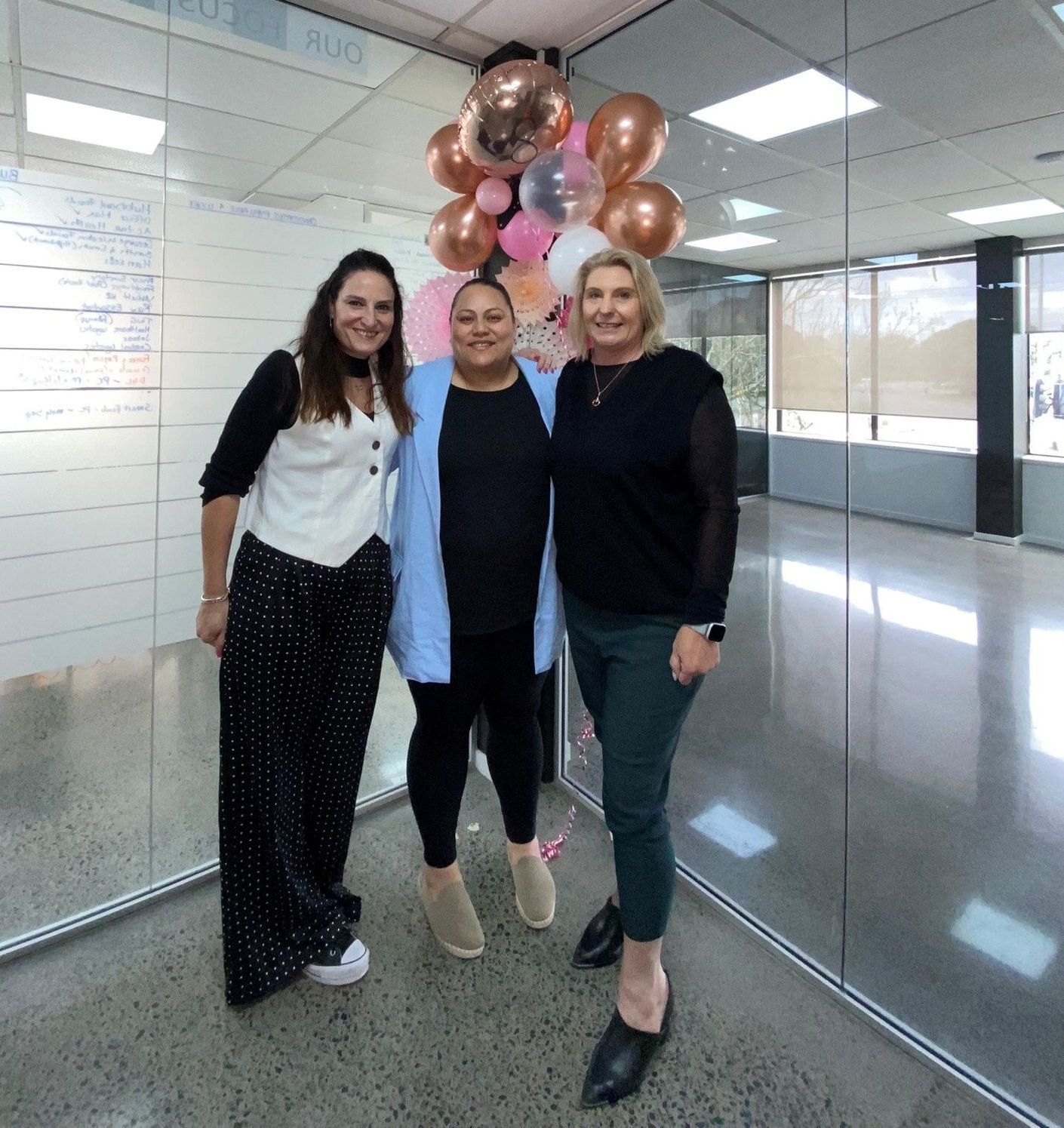 Three women are posing for a picture with balloons in the background