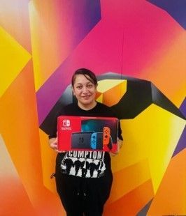 A woman is holding a nintendo switch in front of a colorful wall.