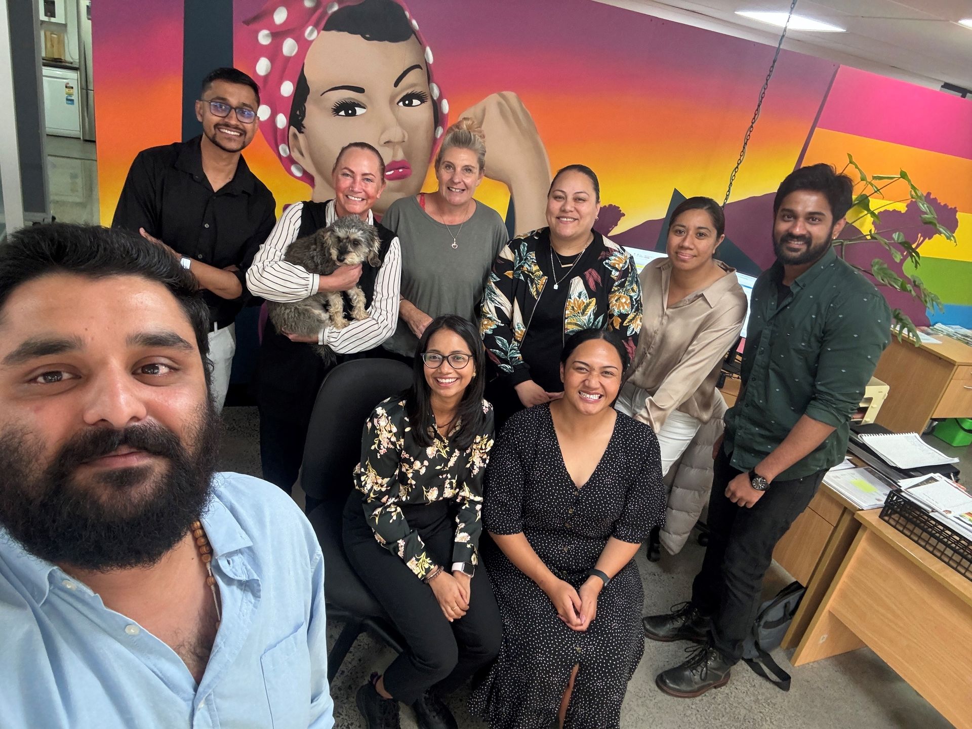 A group of people are posing for a picture in front of a mural.