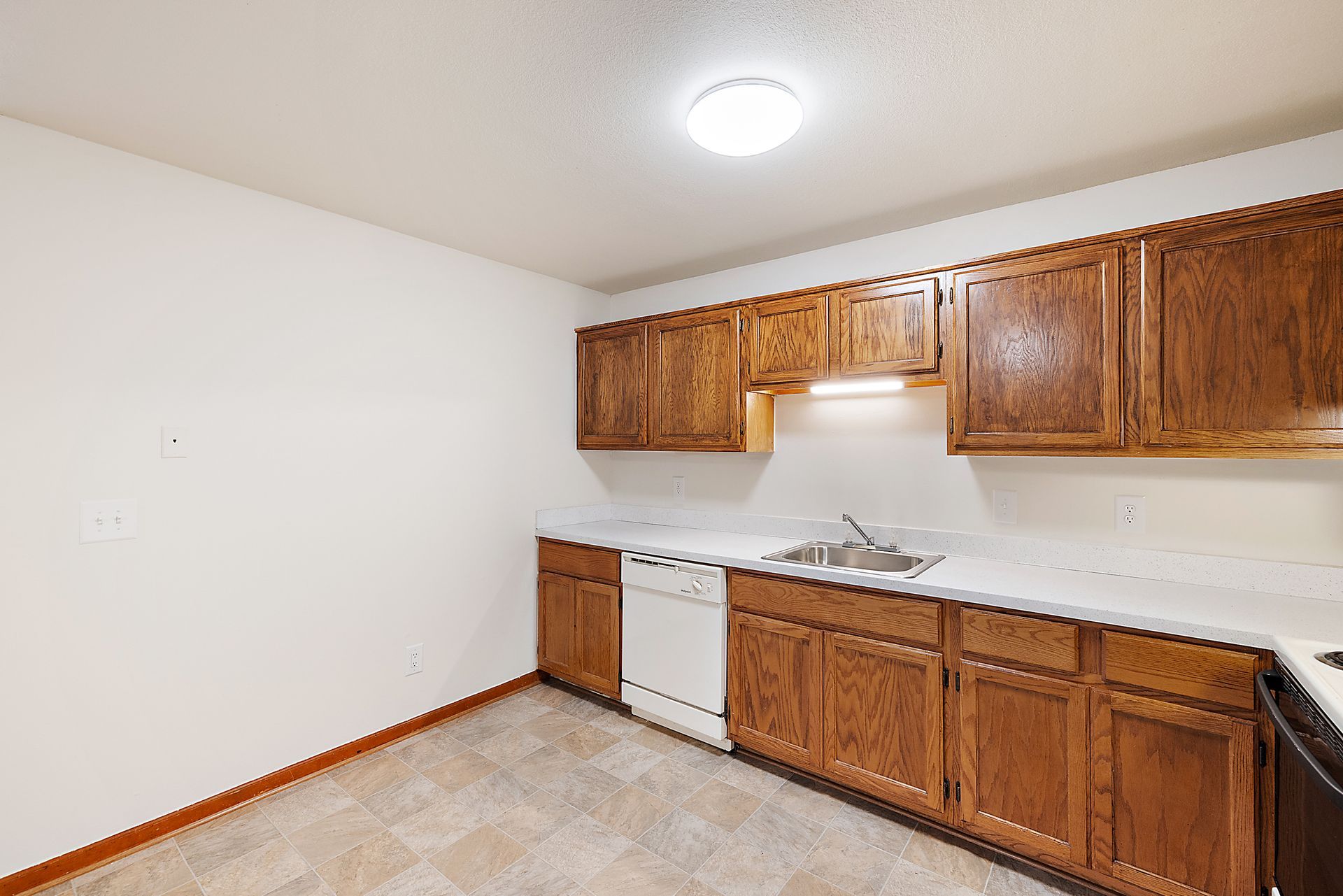 An empty kitchen with wooden cabinets and white counter tops.