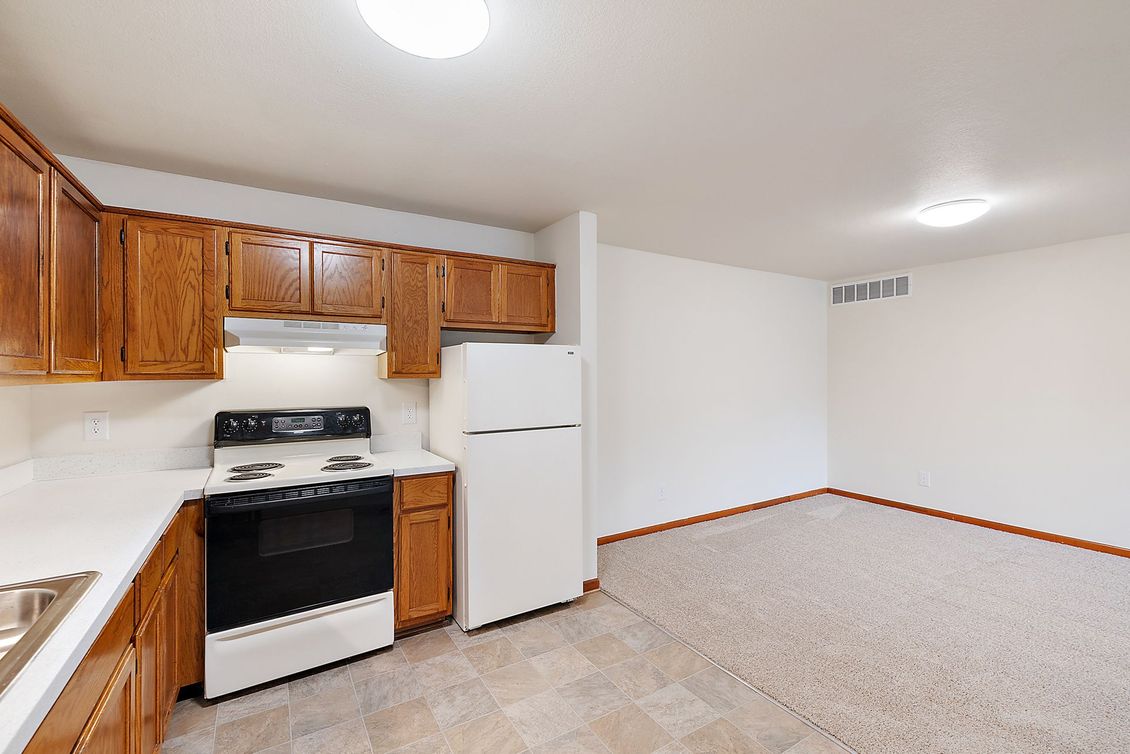 A kitchen with wooden cabinets , a stove , a refrigerator and a sink.