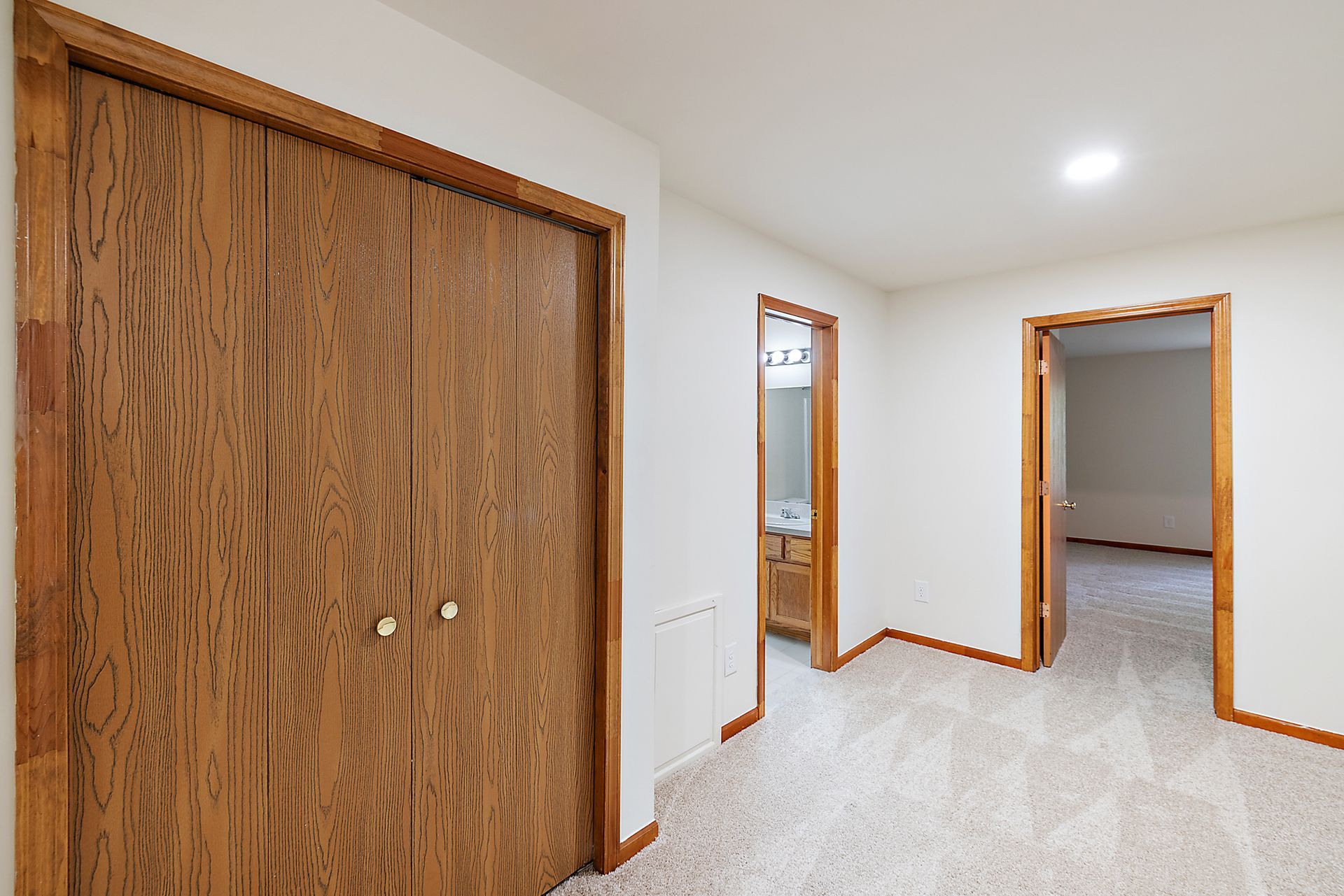 A hallway with wooden doors leading to a bathroom and a bedroom.