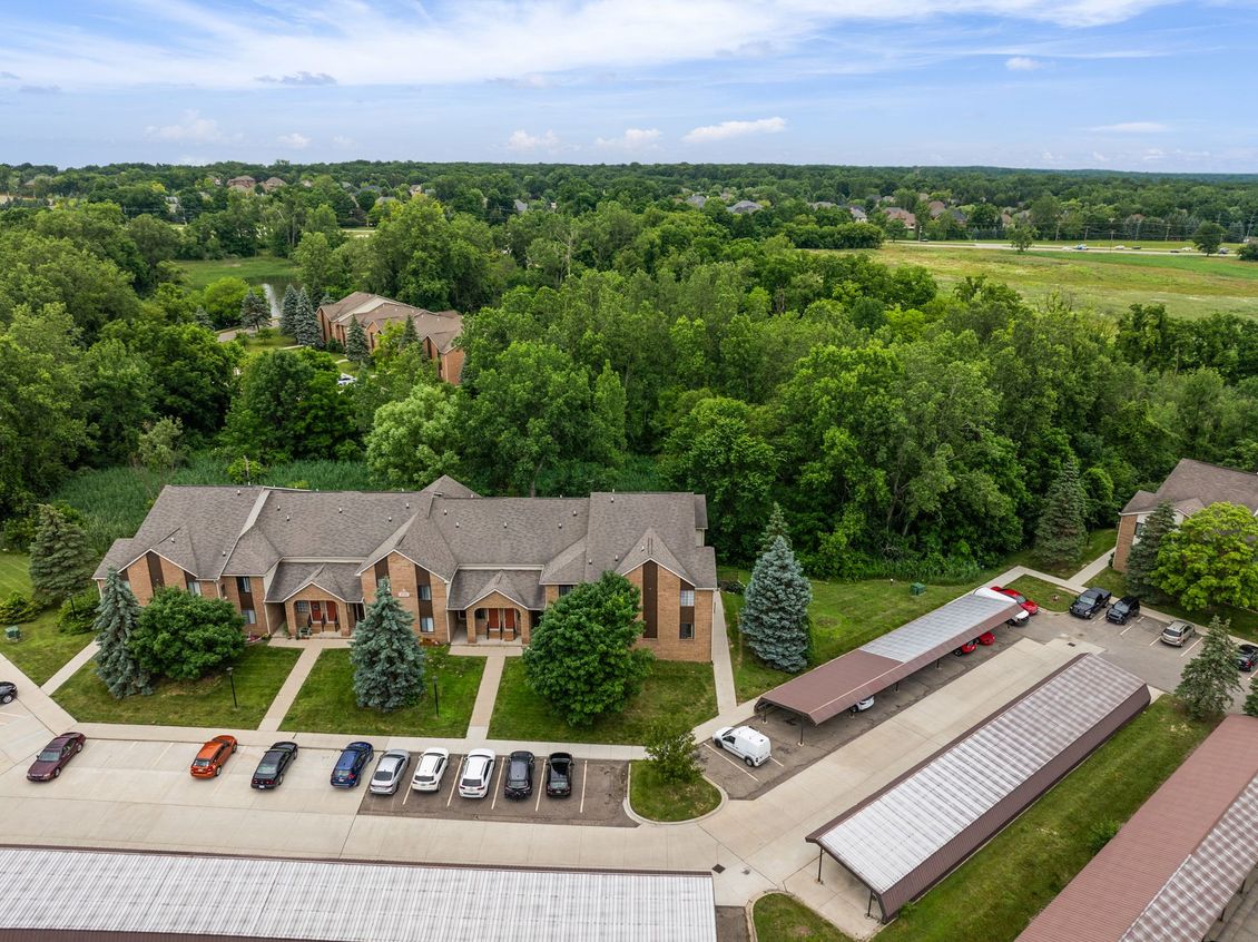 An aerial view of a building with cars parked in front of it surrounded by trees.