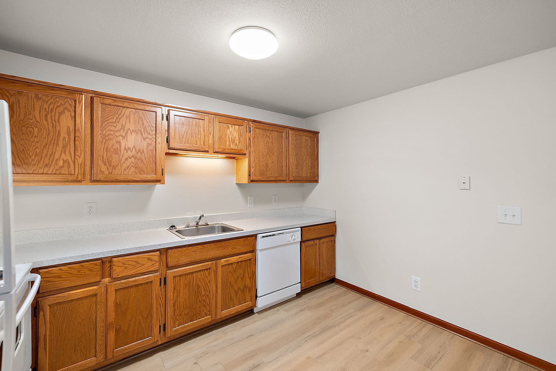A kitchen with wooden cabinets , white appliances , a sink , and a refrigerator.