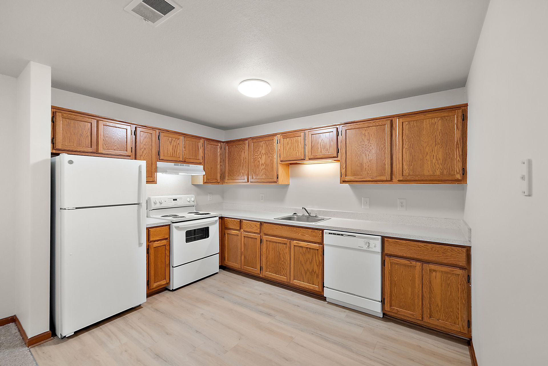 A kitchen with wooden cabinets , white appliances and a refrigerator.
