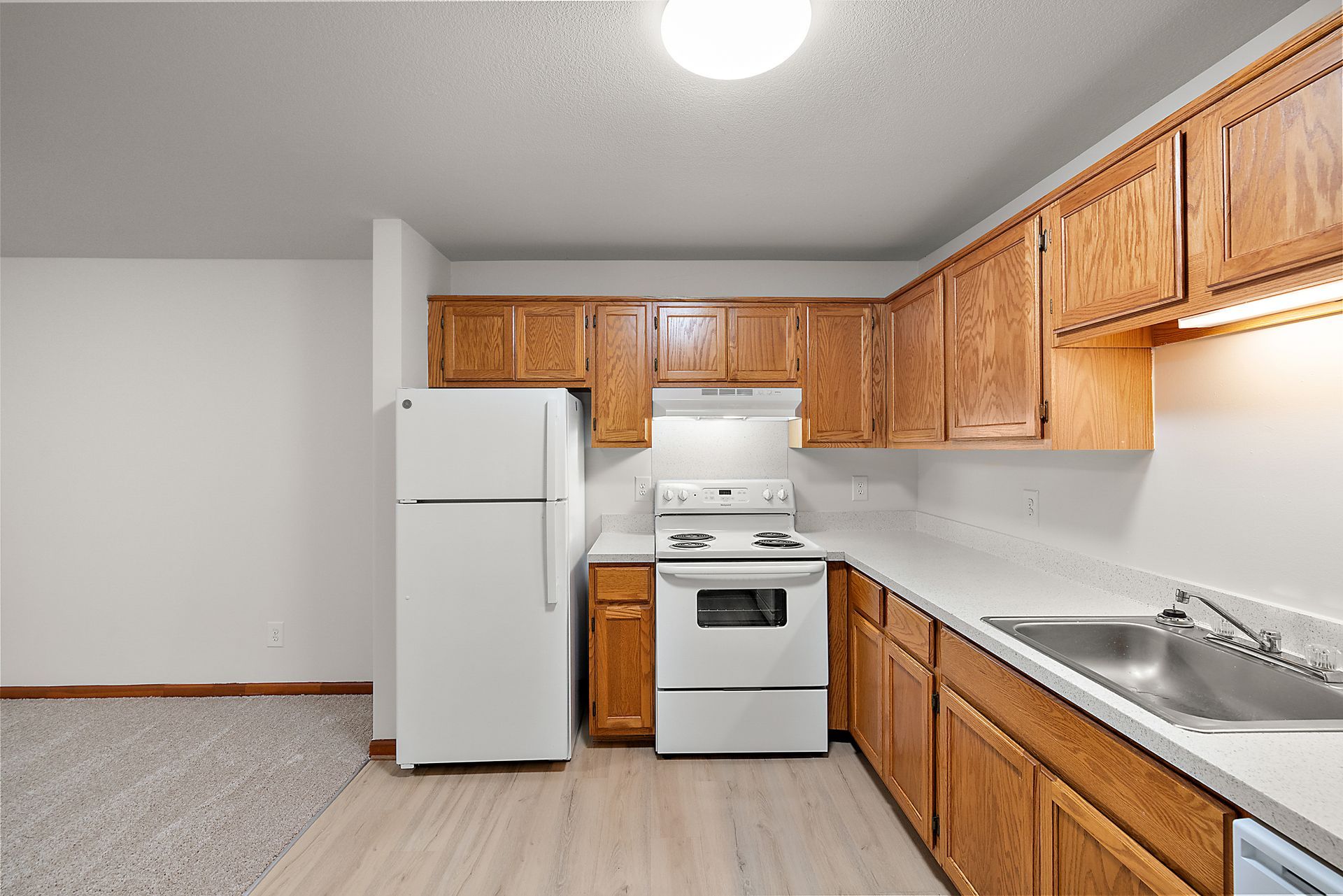 A kitchen with wooden cabinets , a white refrigerator , a stove , and a sink.
