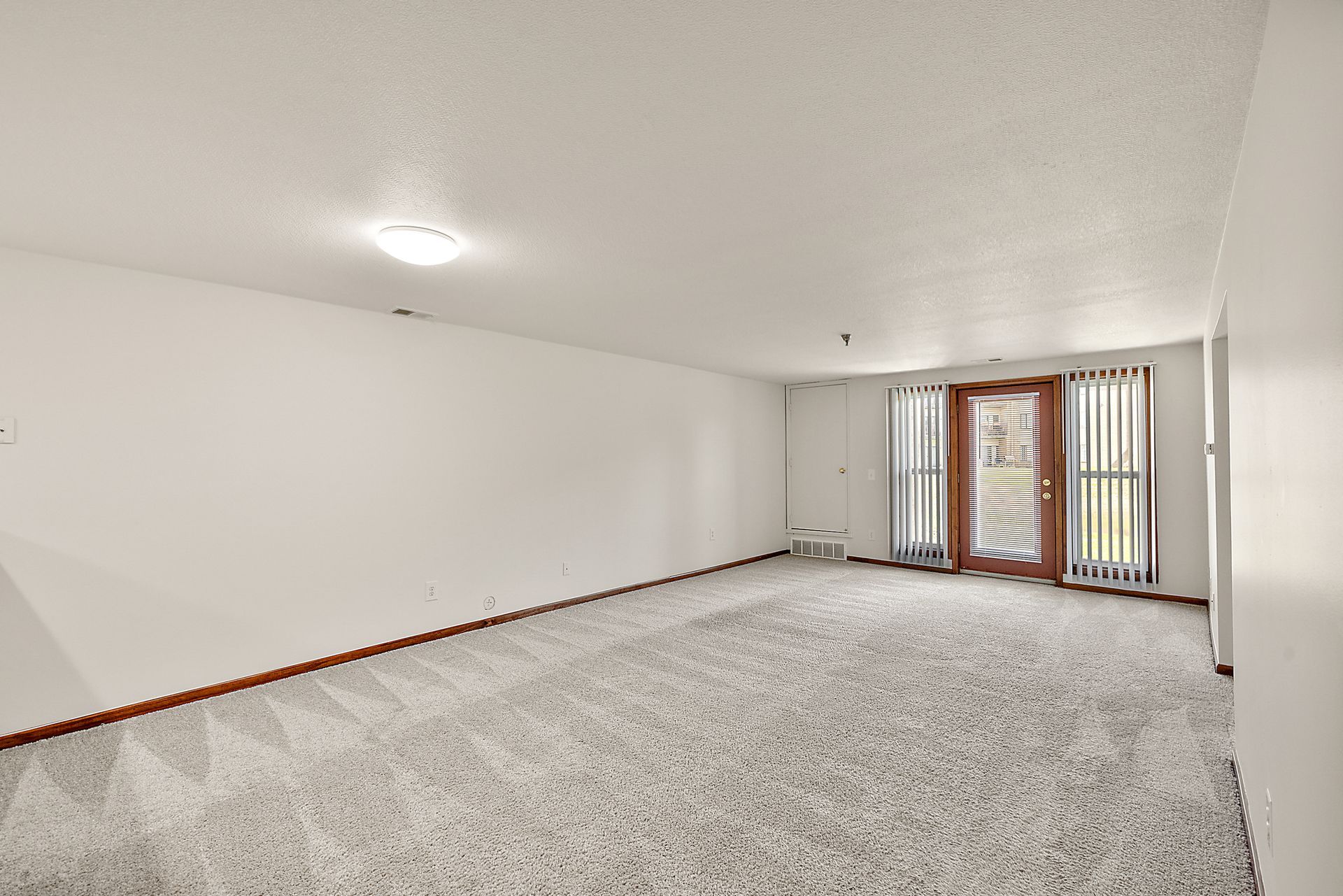 An empty living room with a carpeted floor and a sliding glass door.