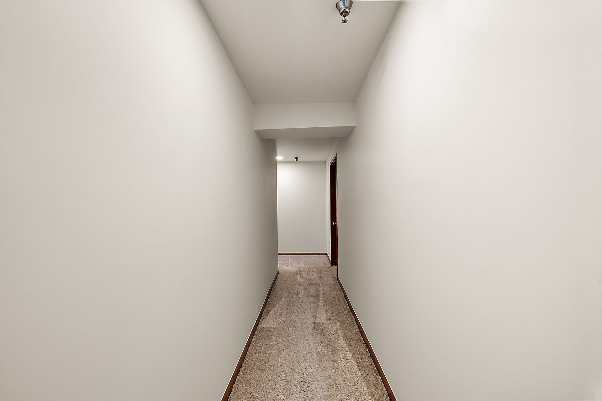 An empty hallway with white walls and a brown door.