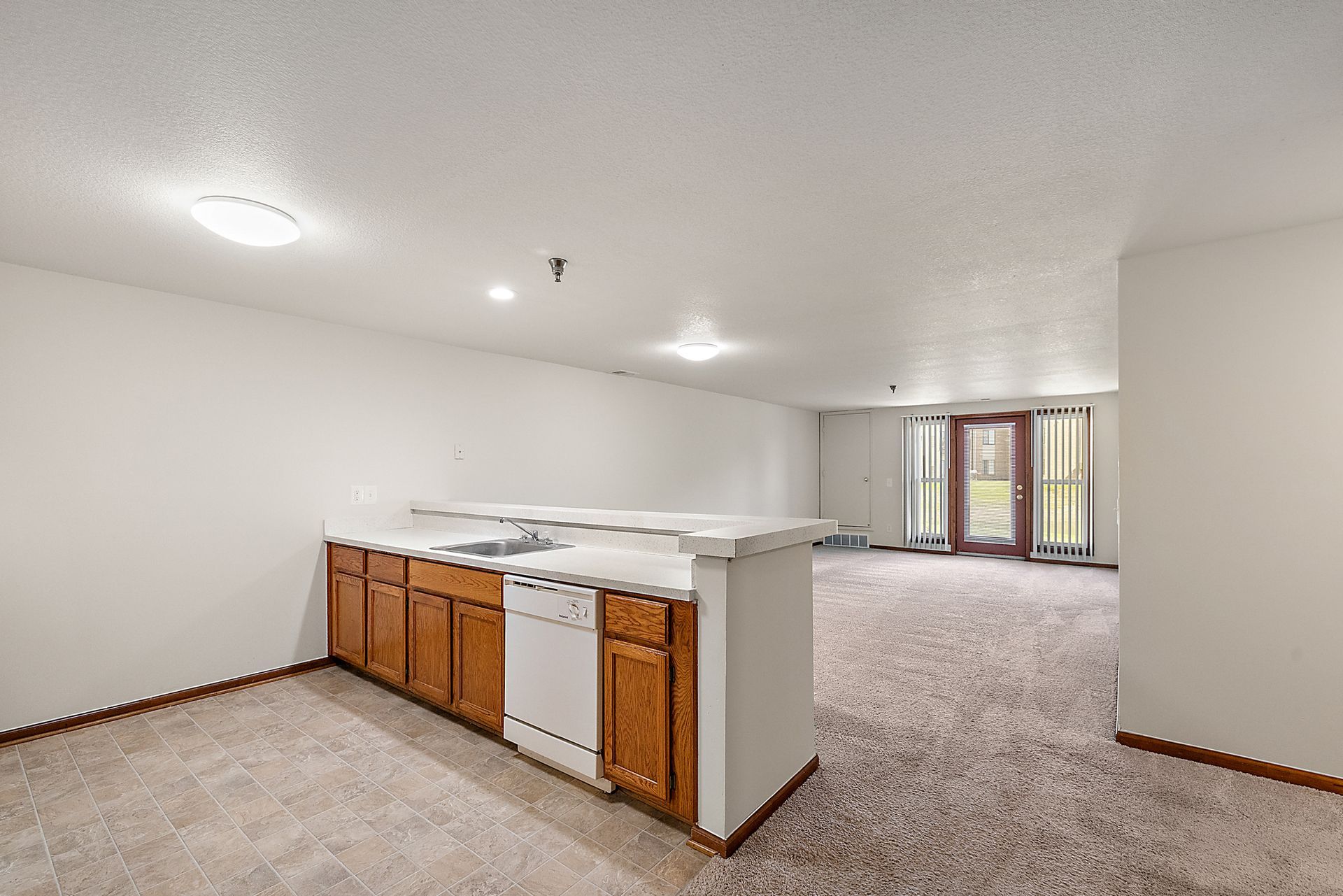 An empty room with a kitchen and a dishwasher in it.