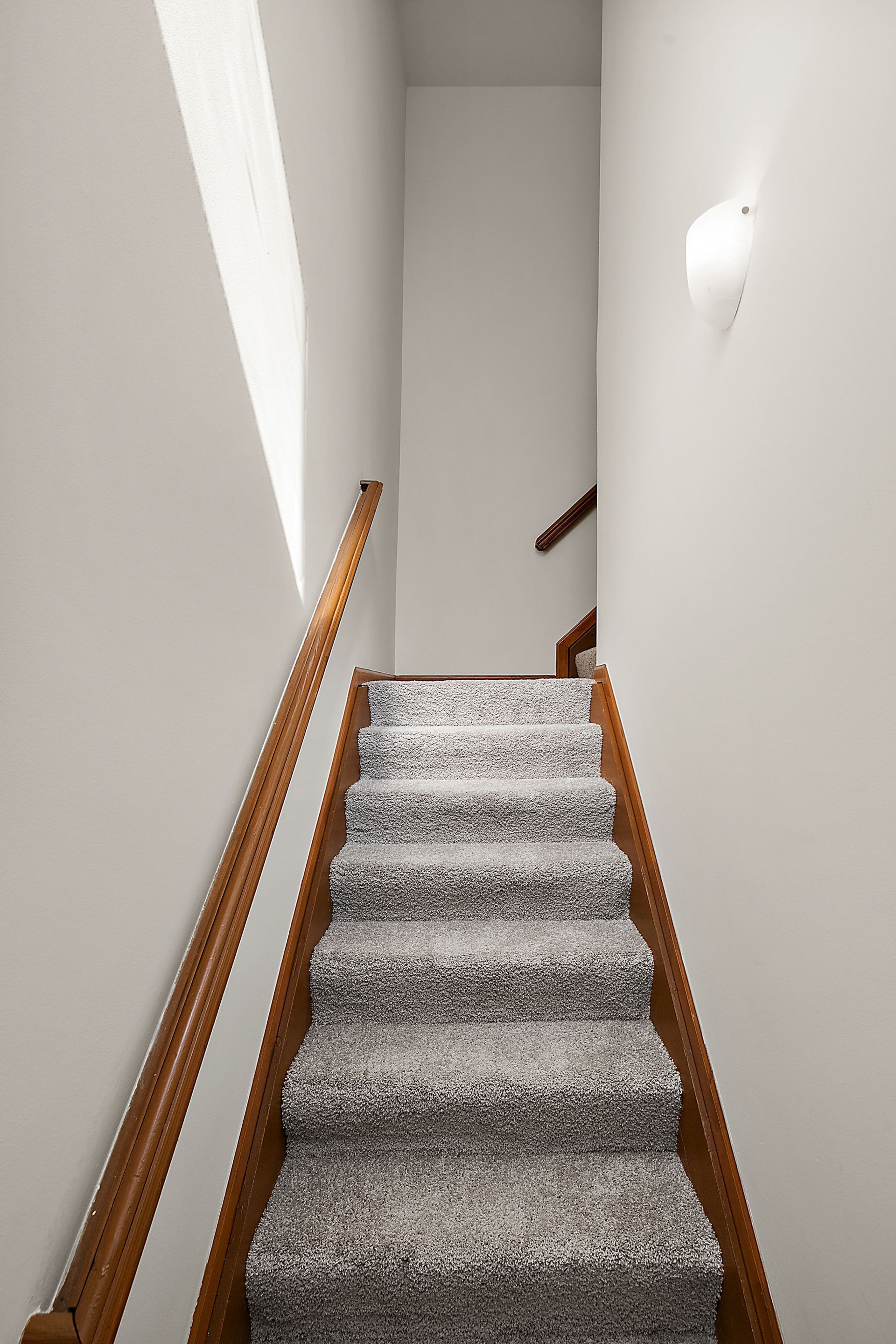 A staircase with a wooden railing and carpeted steps leading up to the second floor.