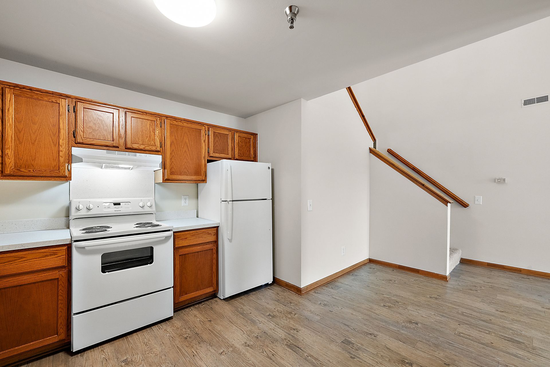 An empty kitchen with a stove , refrigerator , and stairs.