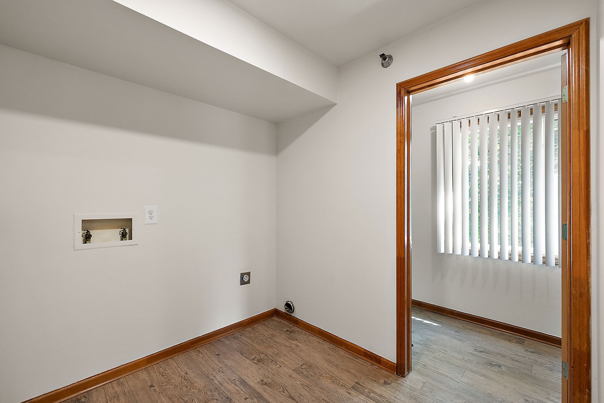 An empty room with a window and a doorway leading to a bedroom.