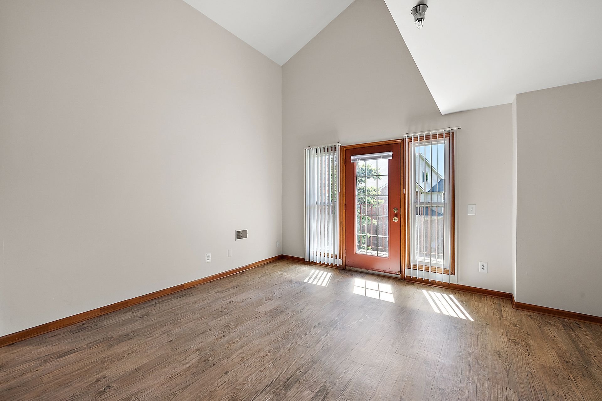 An empty living room with hardwood floors and a sliding glass door.