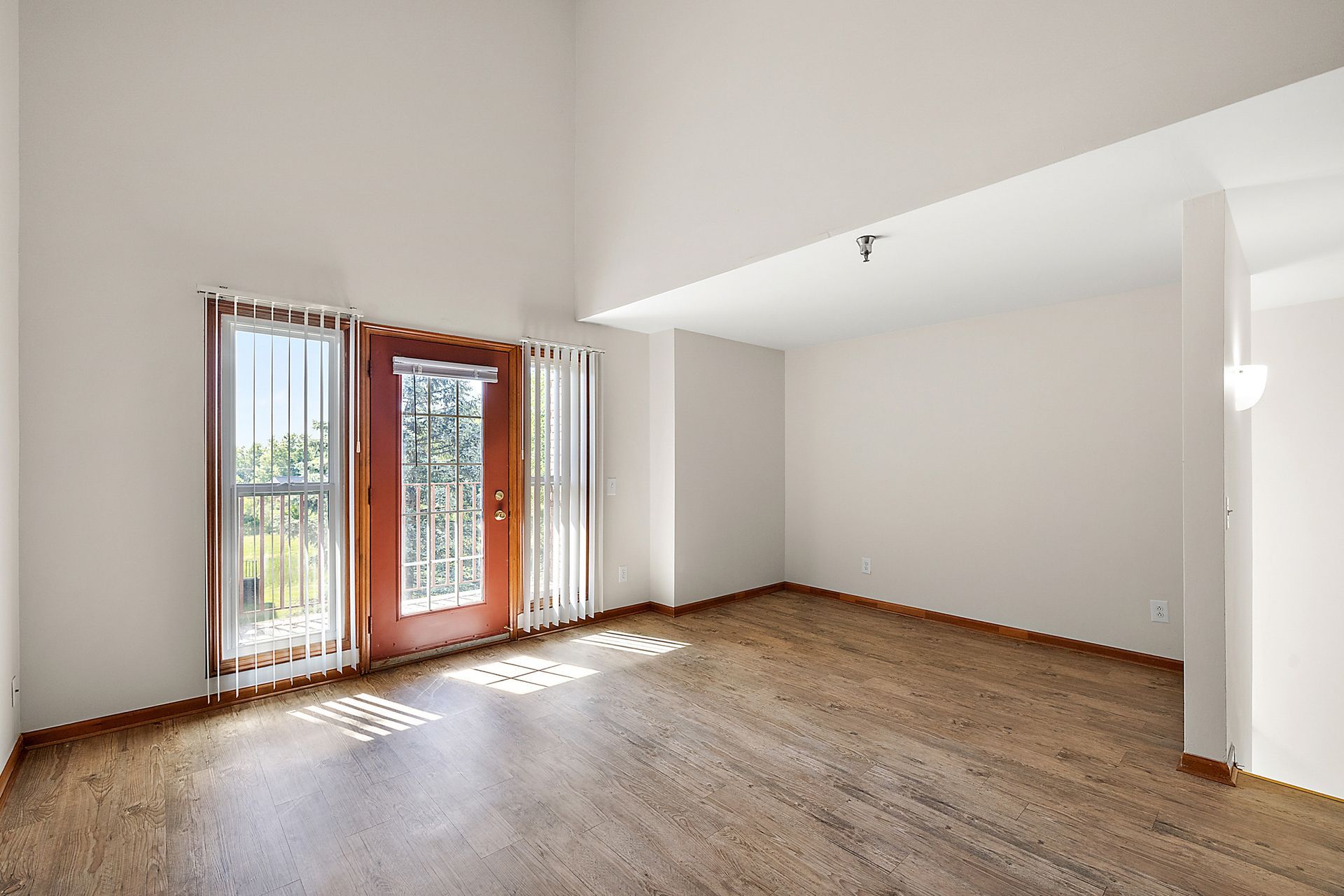 An empty living room with hardwood floors and a sliding glass door.