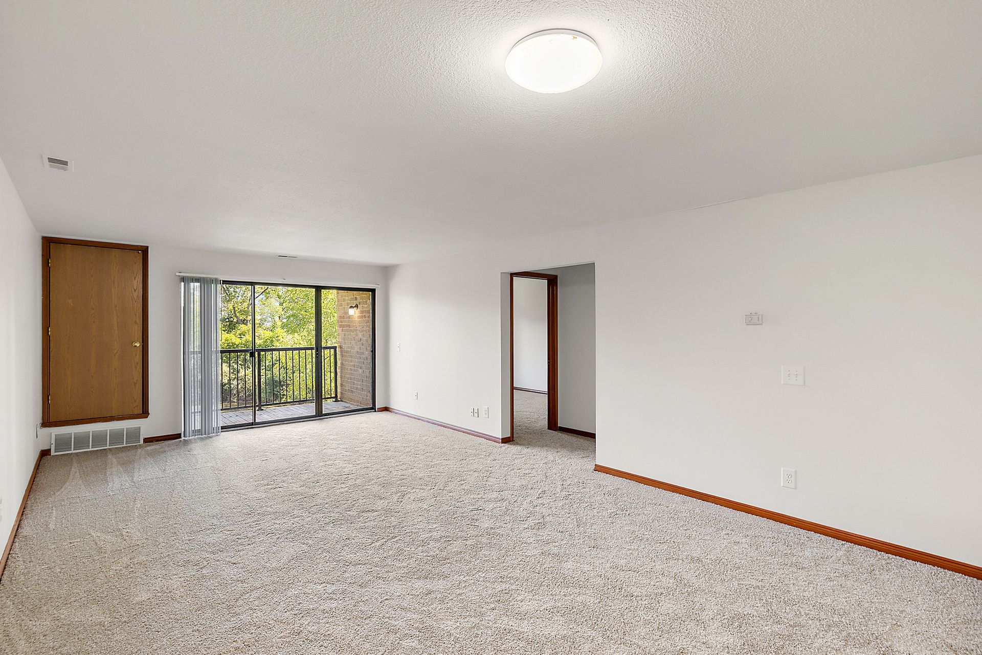 An empty living room with a balcony and sliding glass doors.