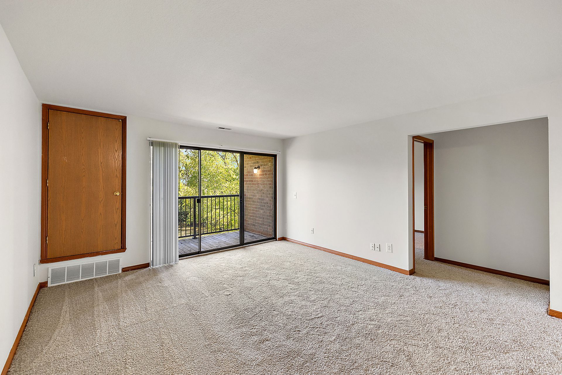 An empty living room with a balcony and sliding glass doors.