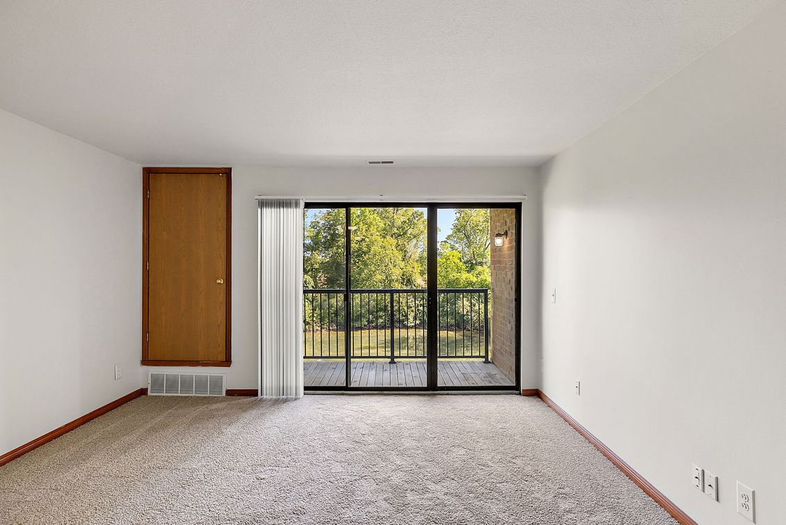 An empty living room with a balcony and sliding glass doors.