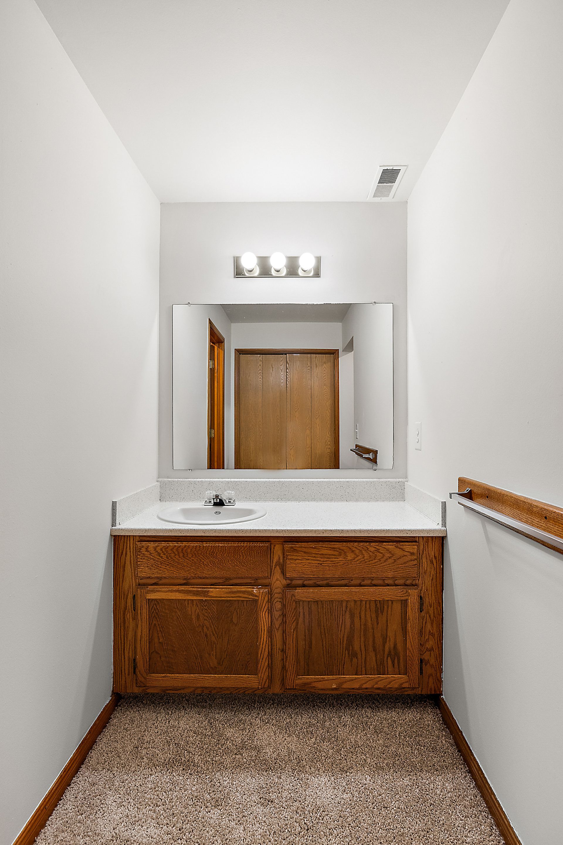 A bathroom with a sink , mirror and wooden cabinets.