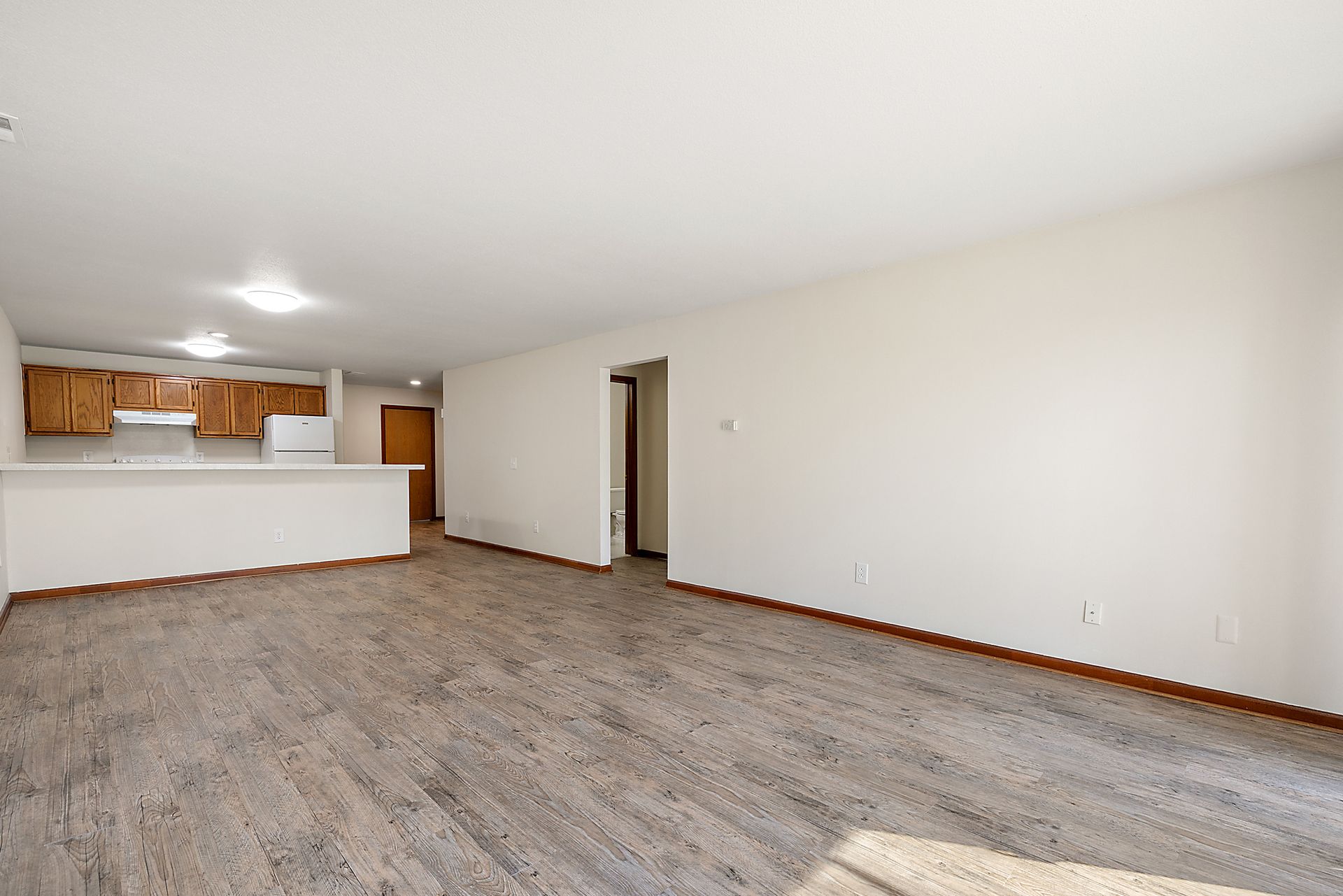 An empty living room with a kitchen in the background.