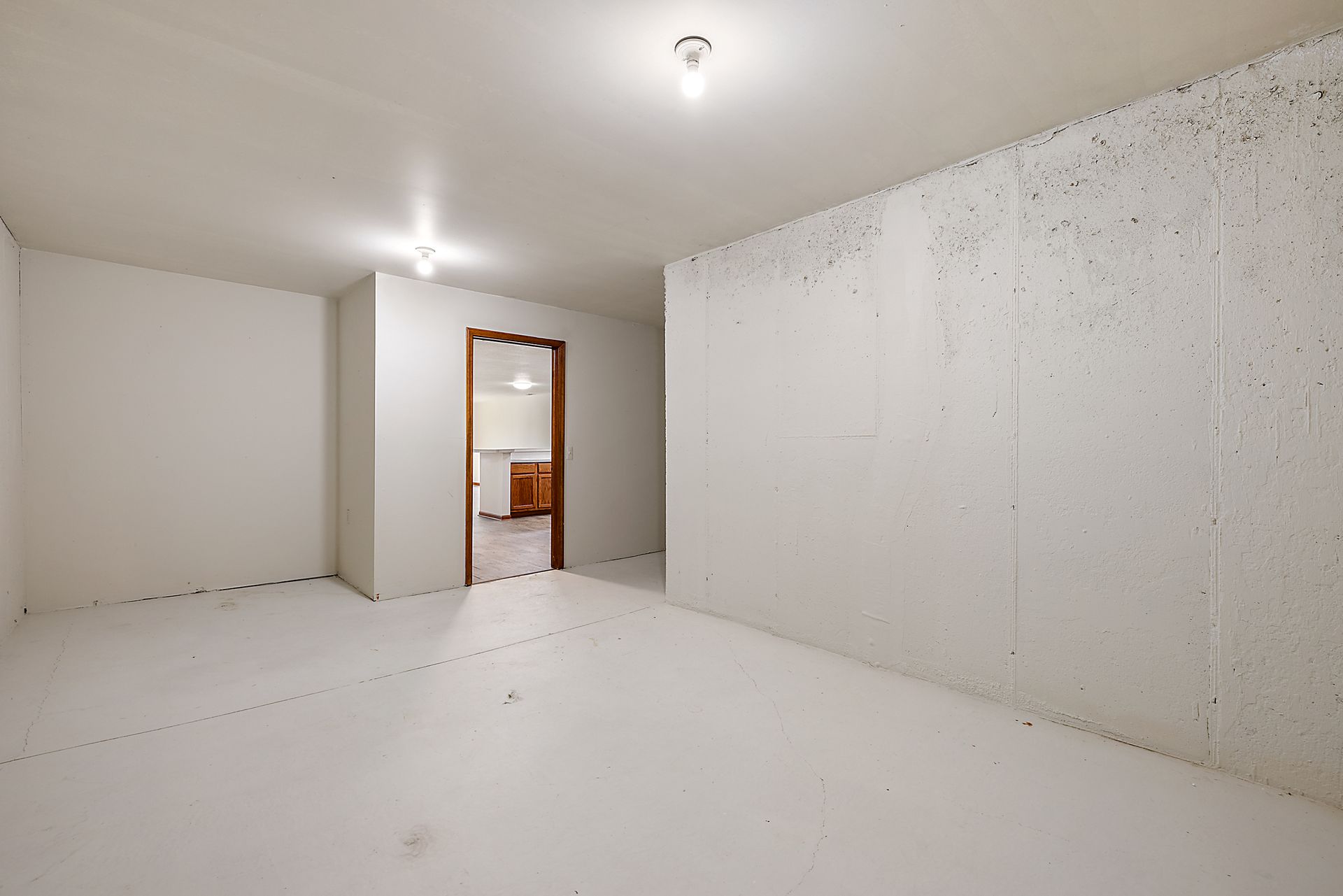 An empty room with white walls and a door leading to a kitchen.