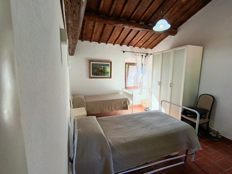 Piccola camera da letto con due letti, armadio bianco, soffitto in legno e pavimento piastrellato.