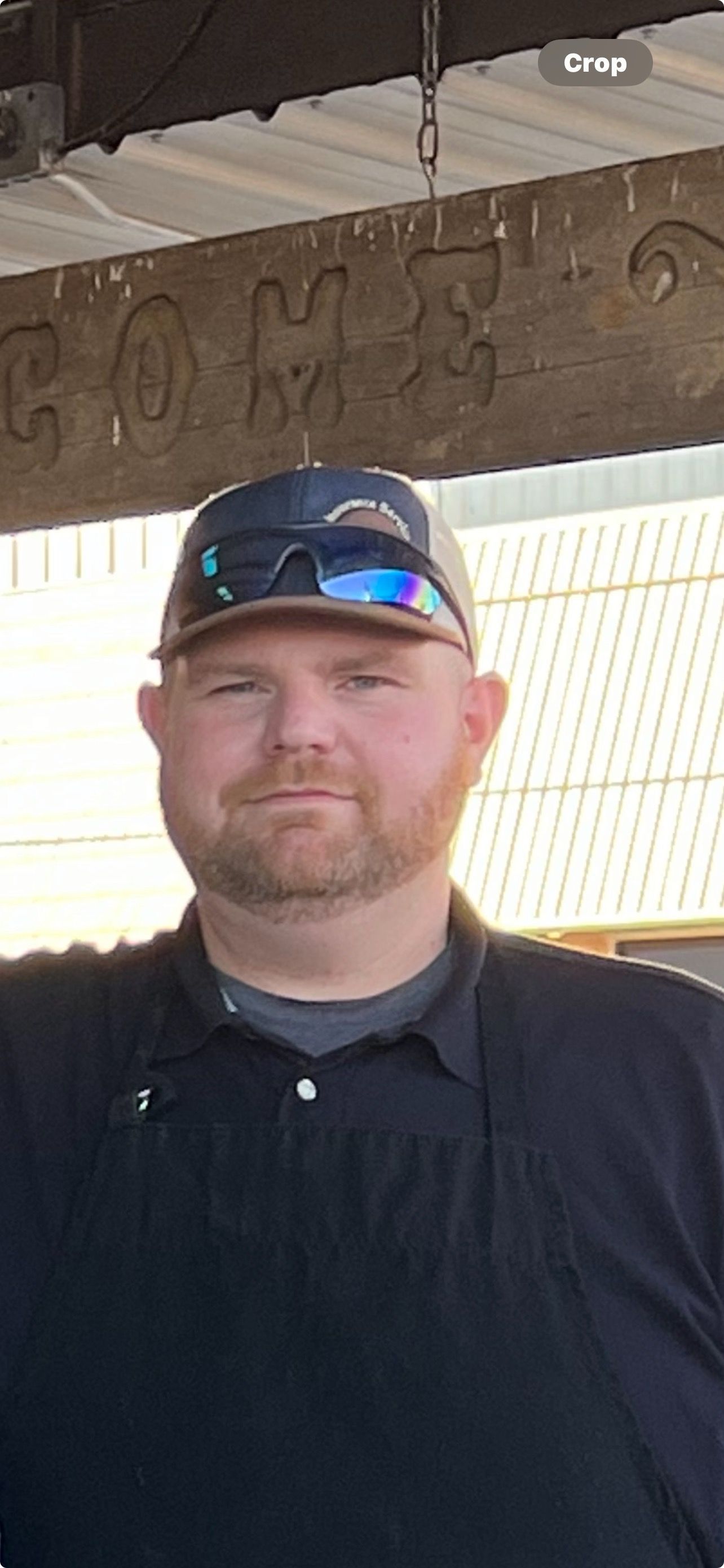A man wearing a hat and sunglasses is standing in front of a wooden sign.
