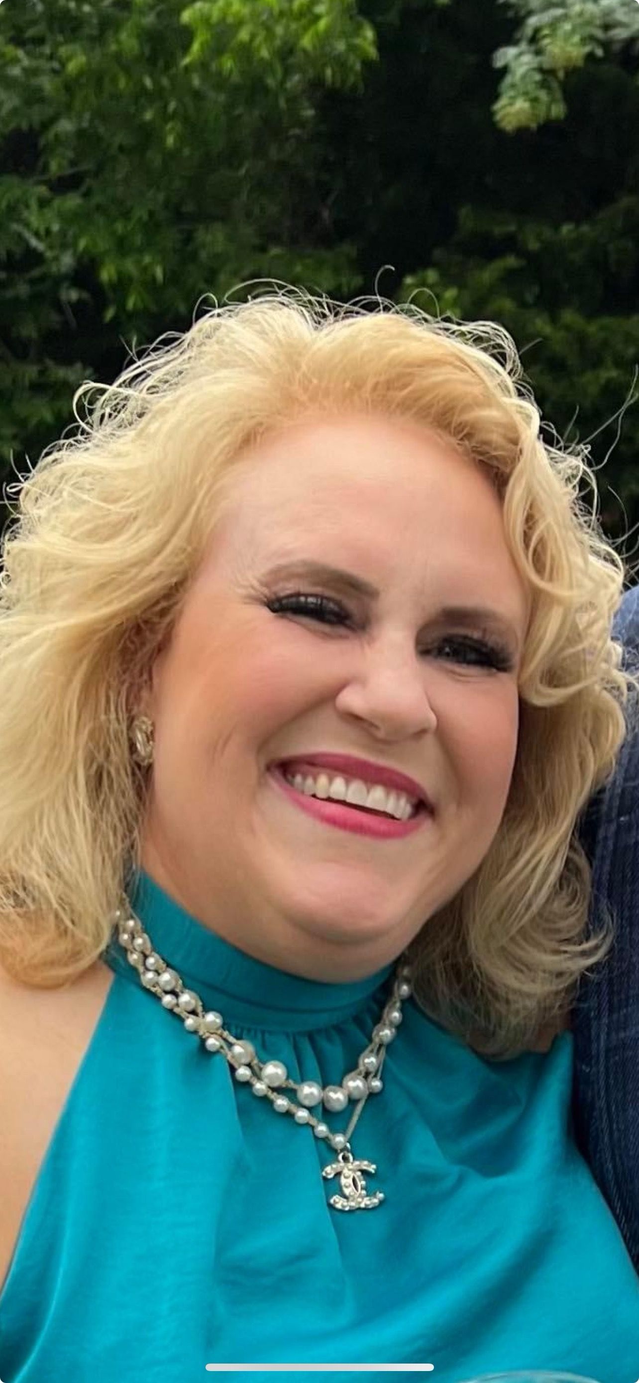 A woman wearing a blue dress and a necklace is smiling.