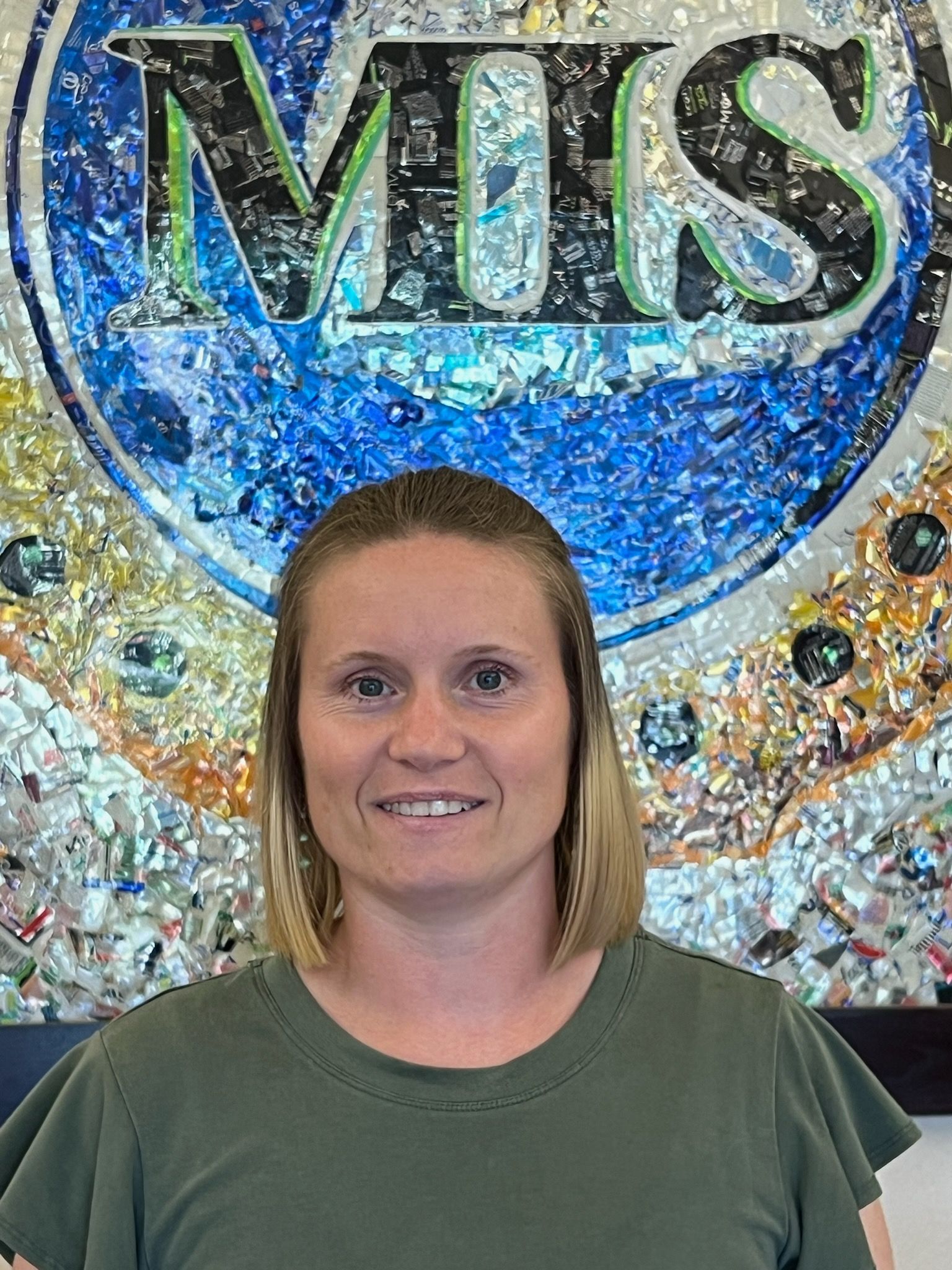 A woman is smiling in front of a mosaic sign.