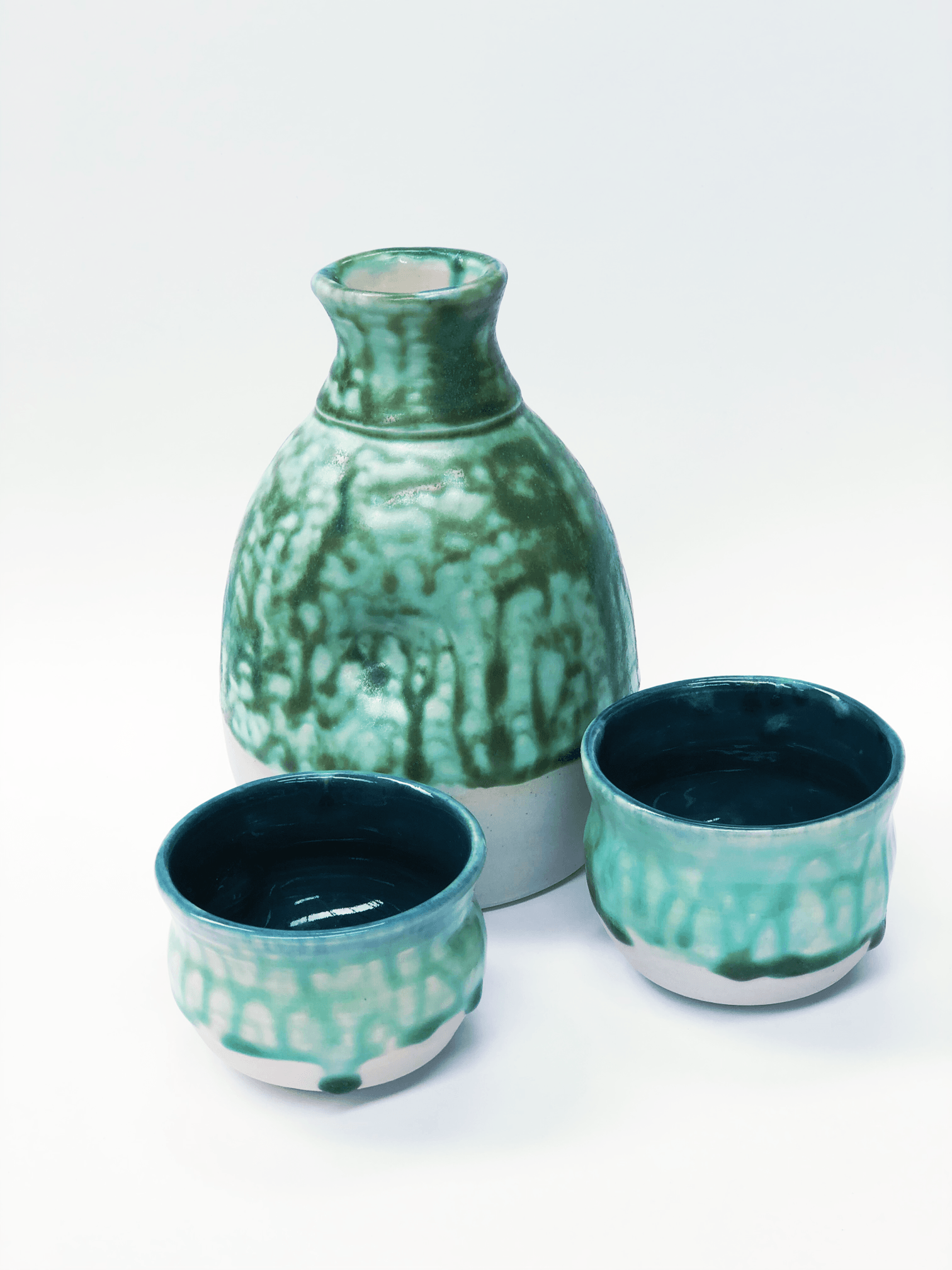 A green vase and two small bowls on a white surface