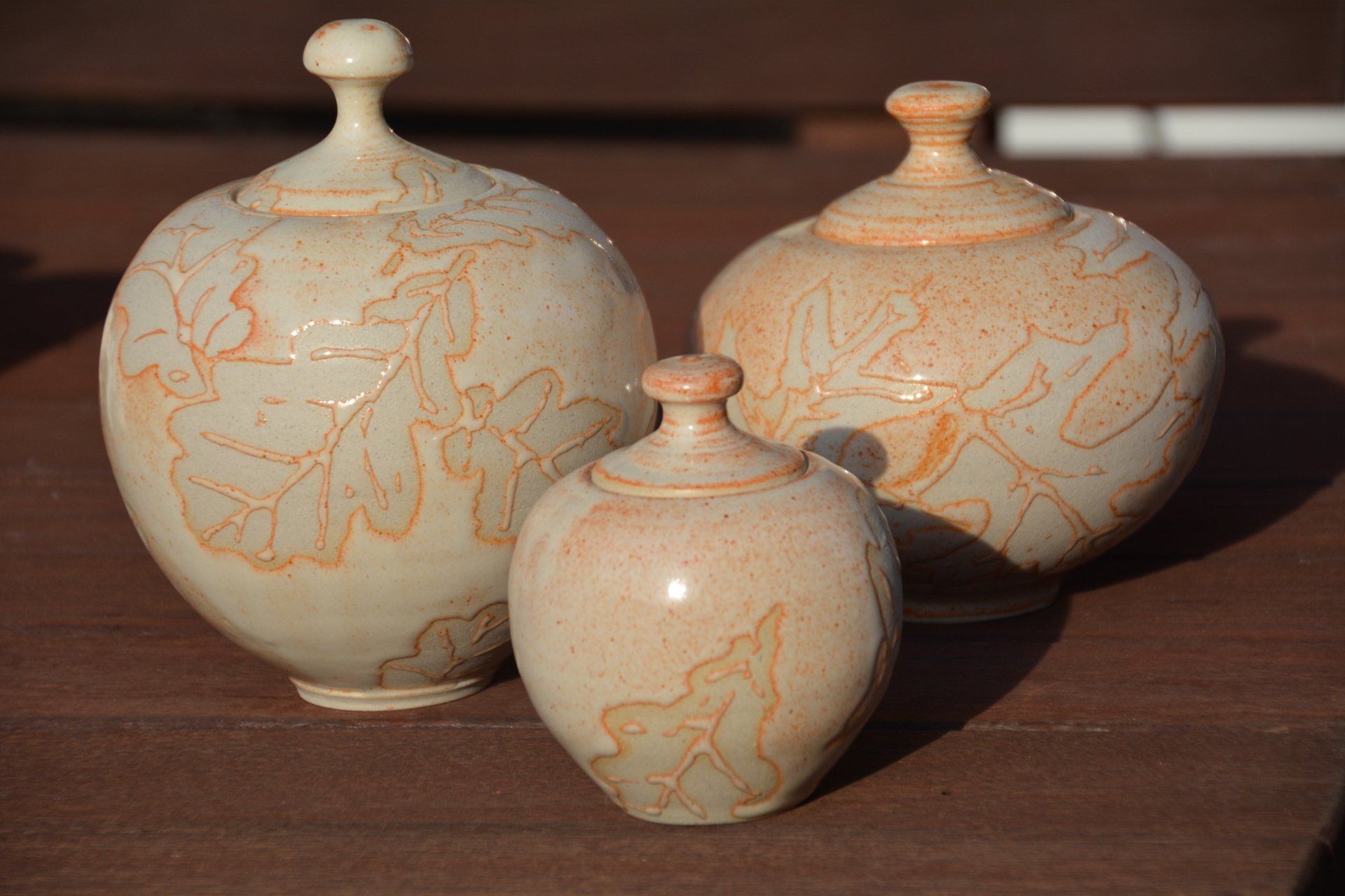 Three vases with lids are sitting on a wooden table.