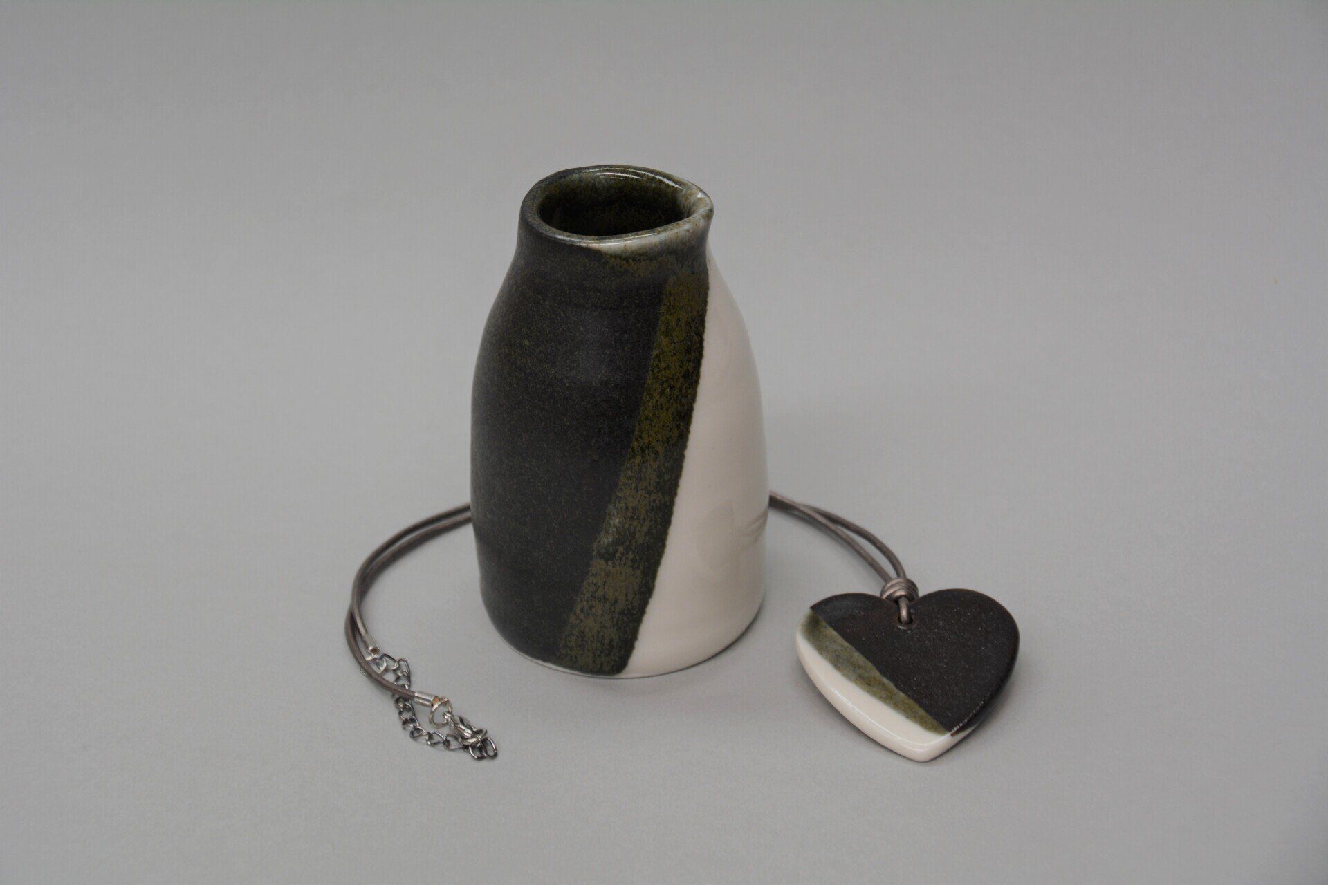 A black and white vase next to a heart shaped pendant