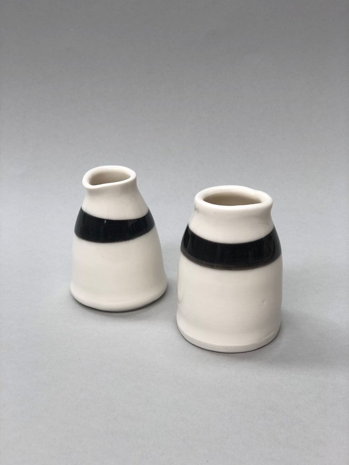 Two small white vases with black stripes on them are sitting on a table.