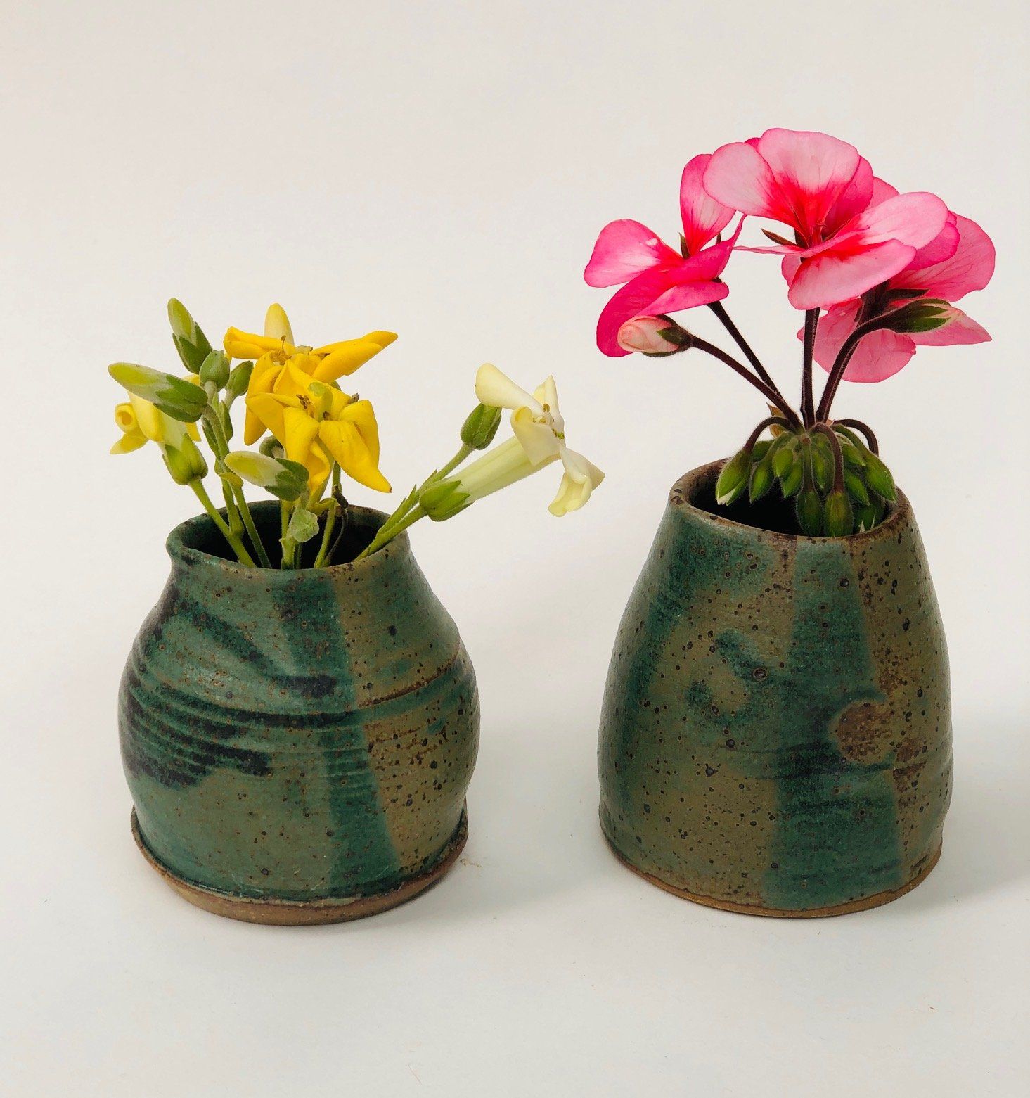 Two green vases with yellow and pink flowers in them