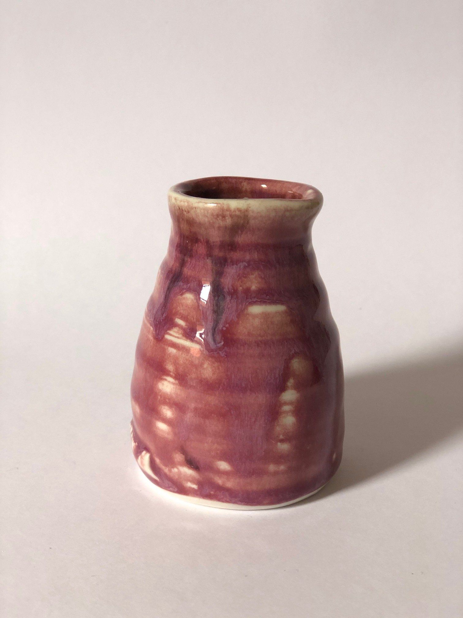 A small pink vase is sitting on a white surface.