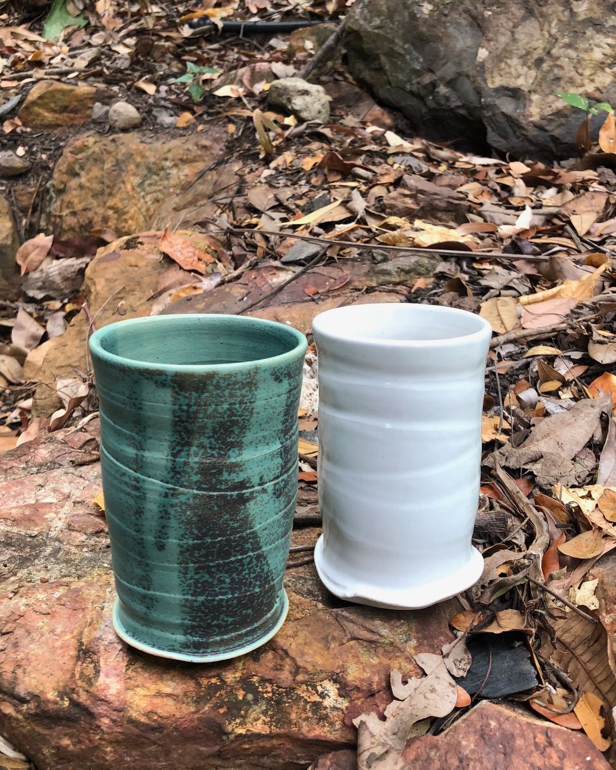 Two ceramic cups are sitting on top of a rock.