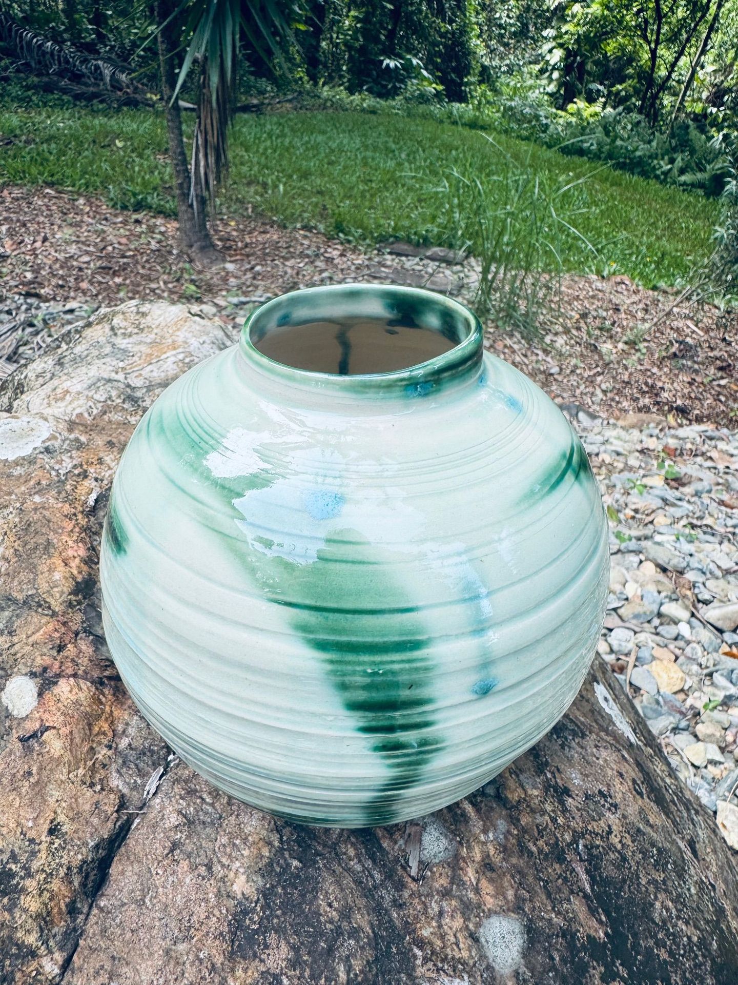 A green and white vase is sitting on top of a rock.