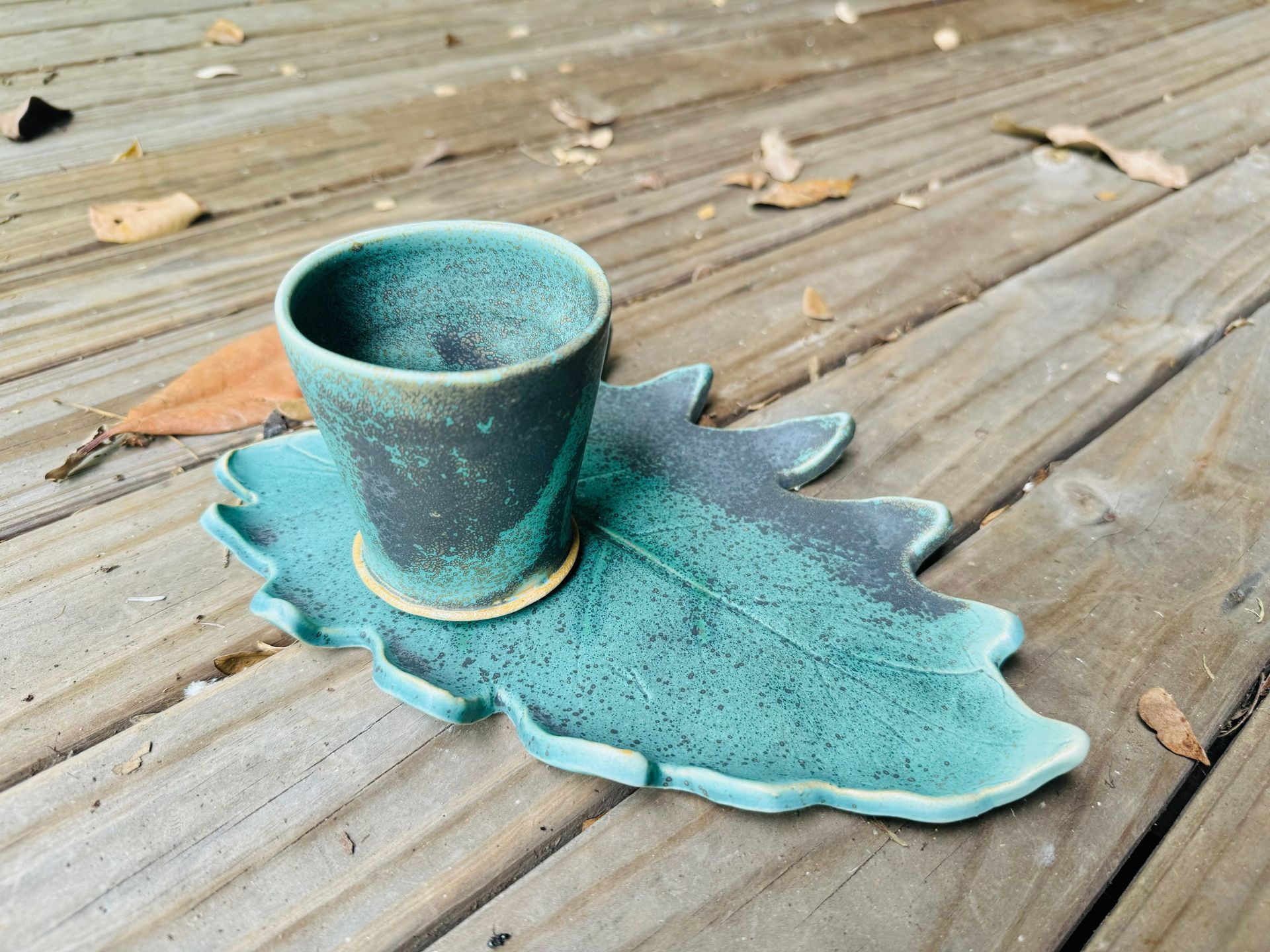 A cup and saucer shaped like a leaf are on a wooden table.