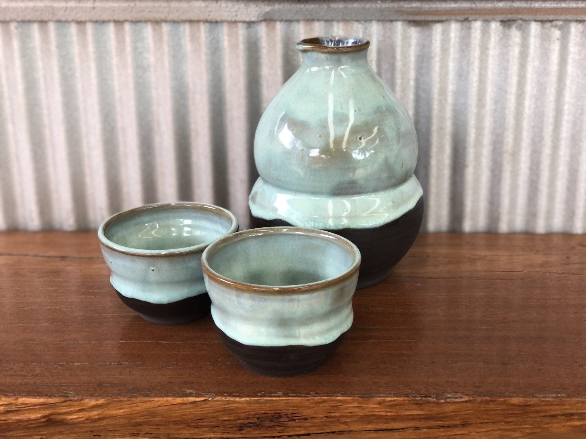 A bottle and two cups are sitting on a wooden table.