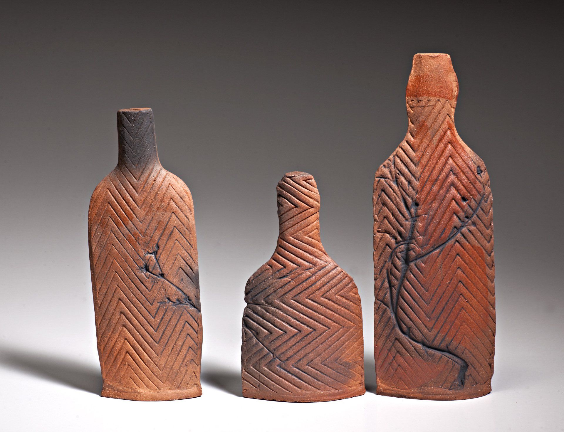 Three clay bottles are lined up on a white surface