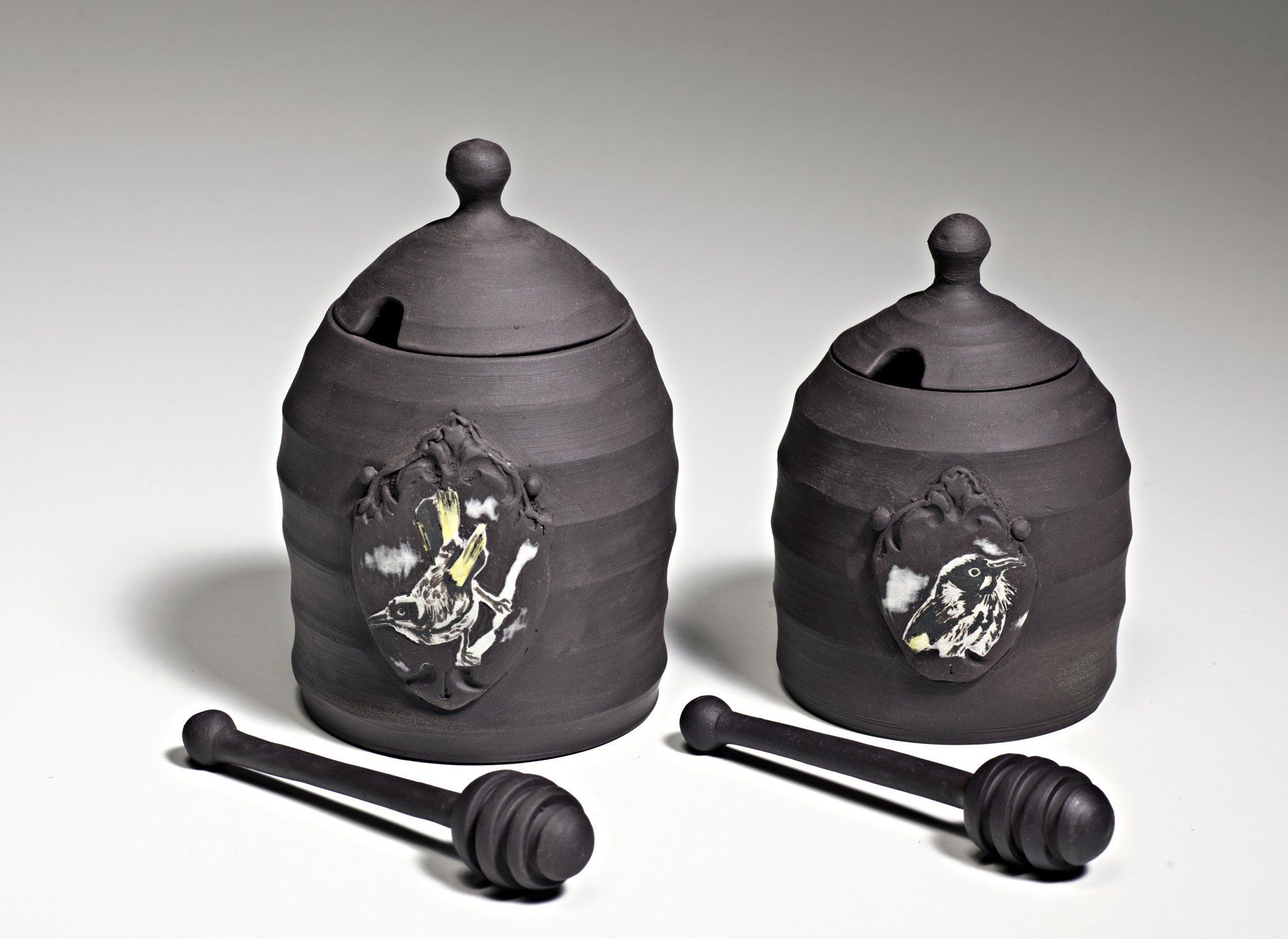 Two black beehive shaped jars with lids and honey dippers